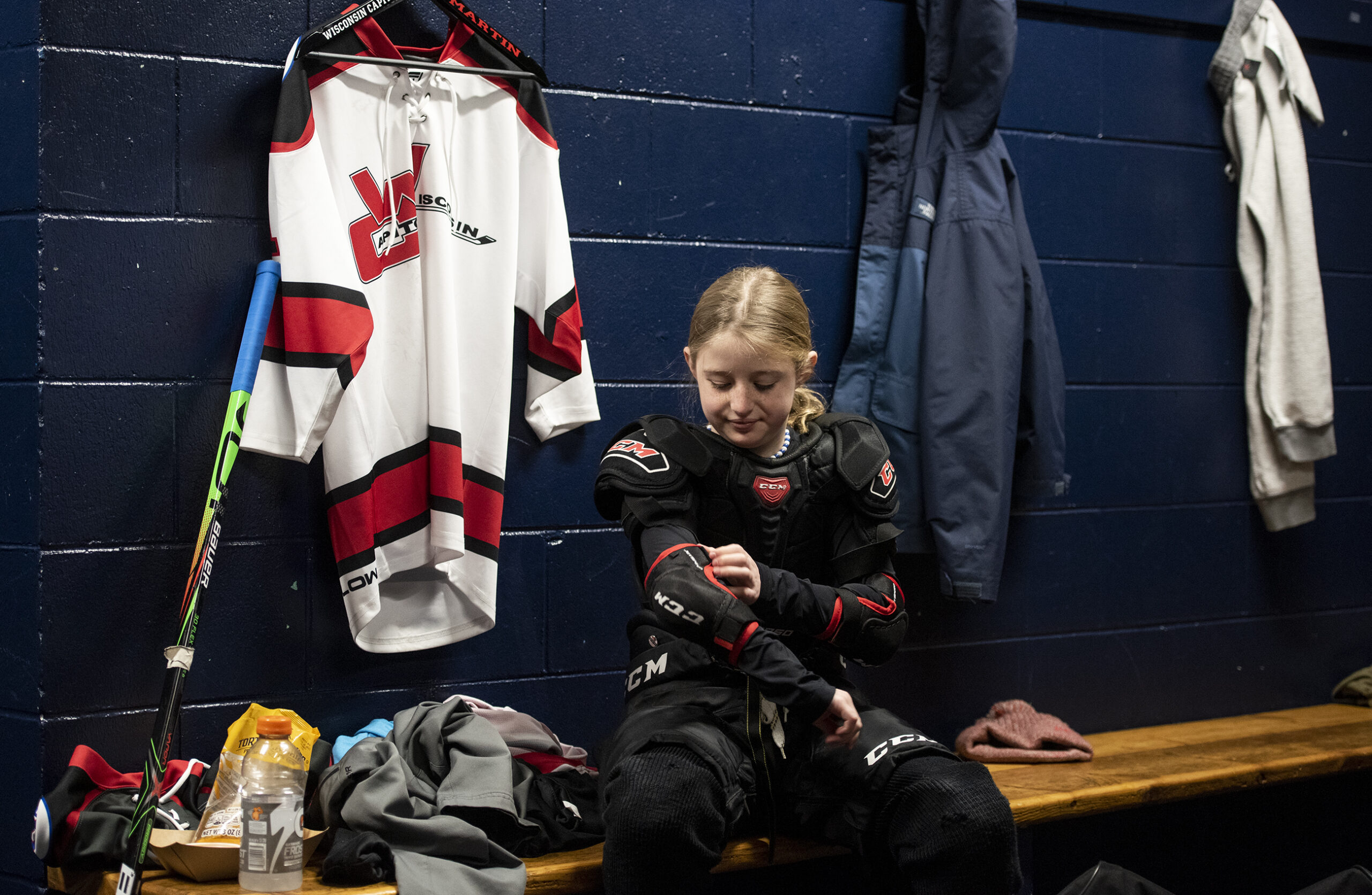 A girl in a locker room puts pads on before practice.