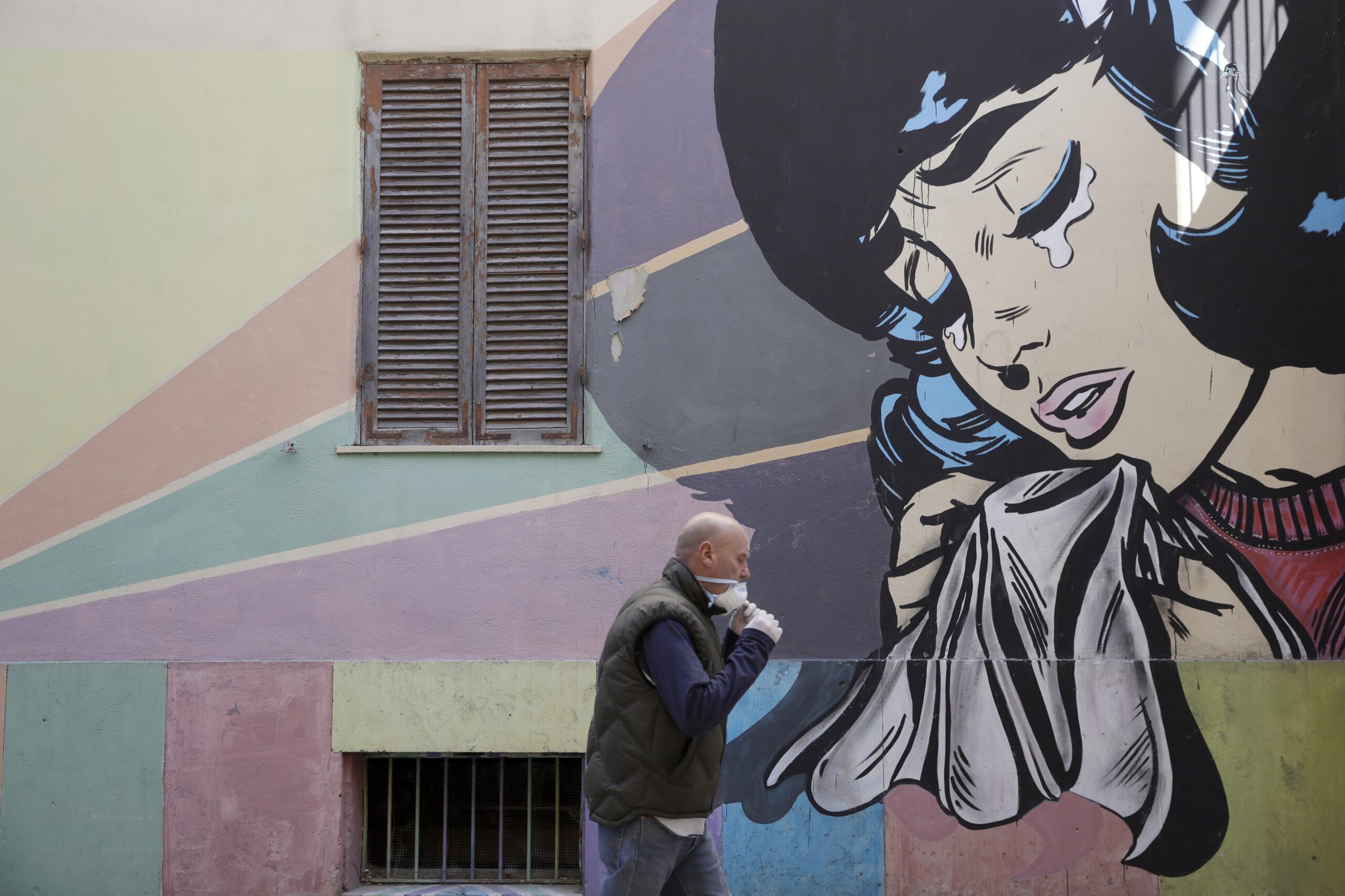 A man adjusts his face mask as he walks past a mural of a crying woman