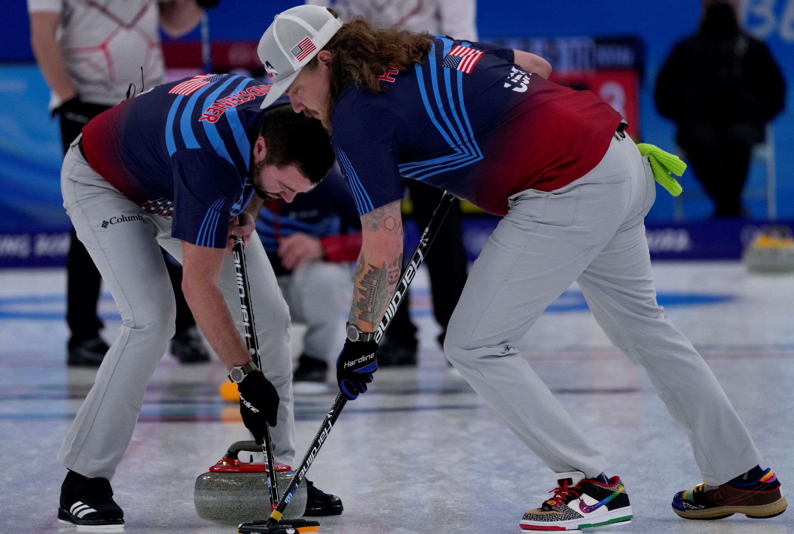 Two men from the U.S. Olympic curling team push a curling stone