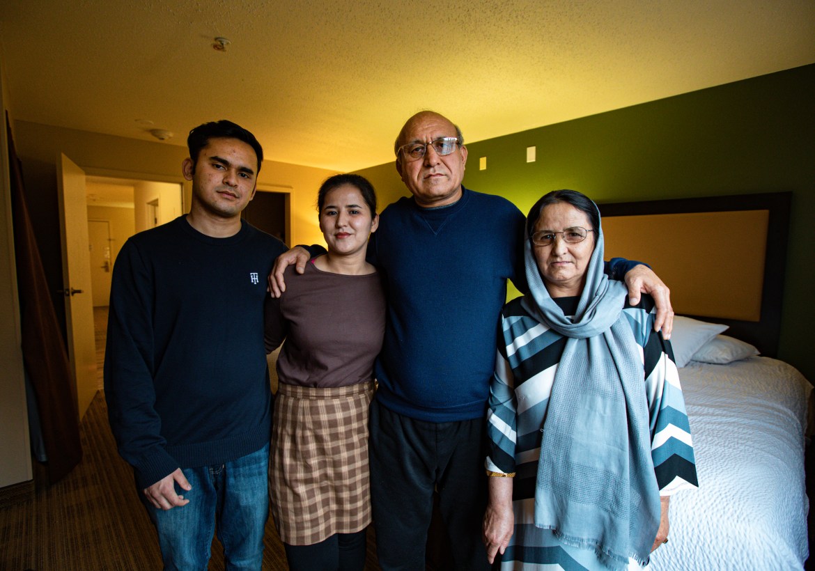 A family of four stands side by side in a hotel room