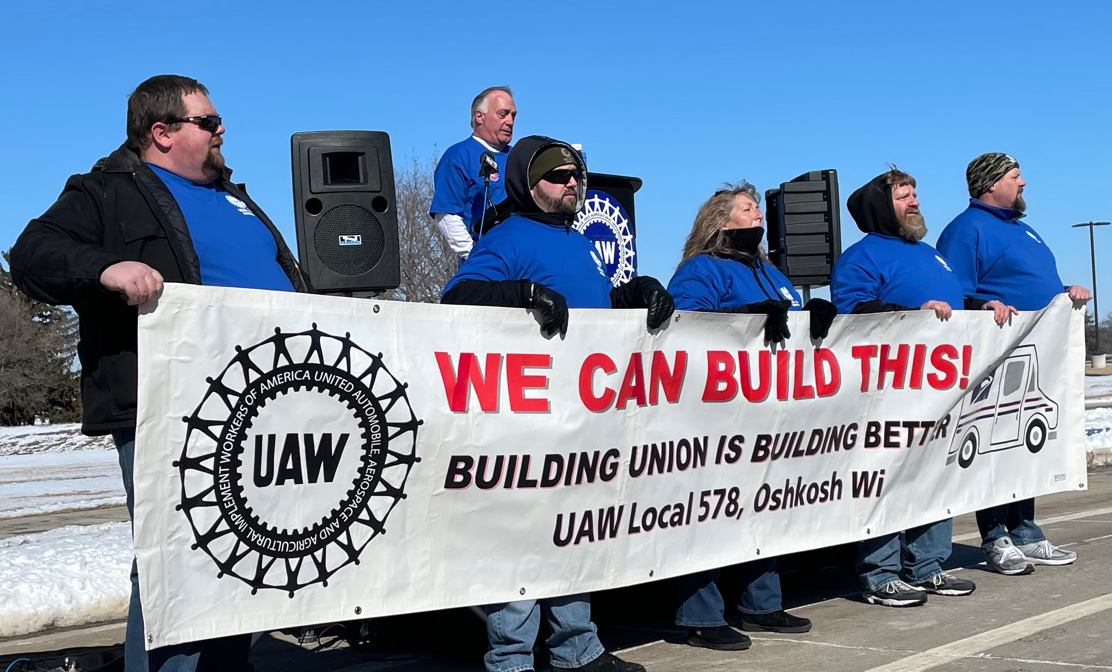 United Auto Workers union members hold a banner at a rally in Oshkosh as local union president Bob Lynk speaks