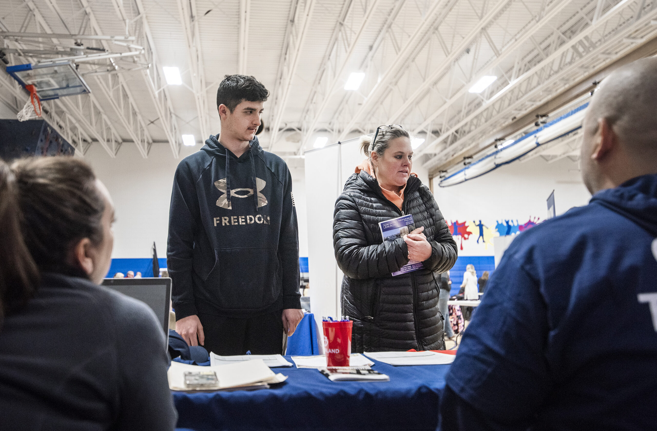 A student and his mother stop by a booth to talk to people at a career fair.