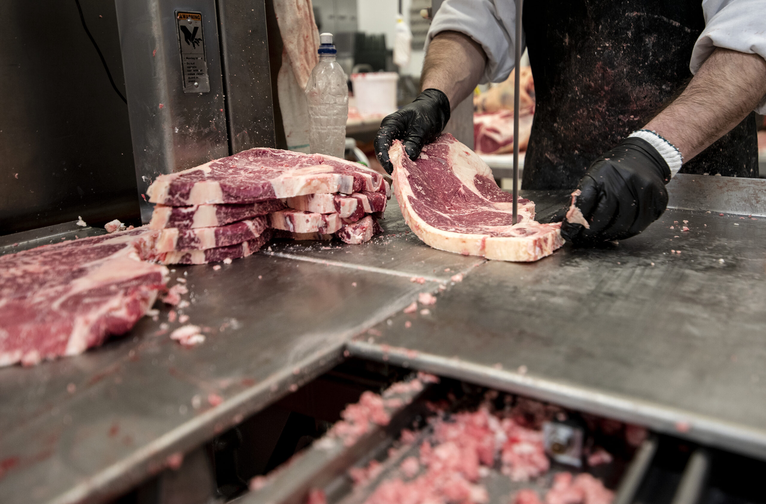 A worker wears black gloves as he slides a piece of meat into a band saw blade