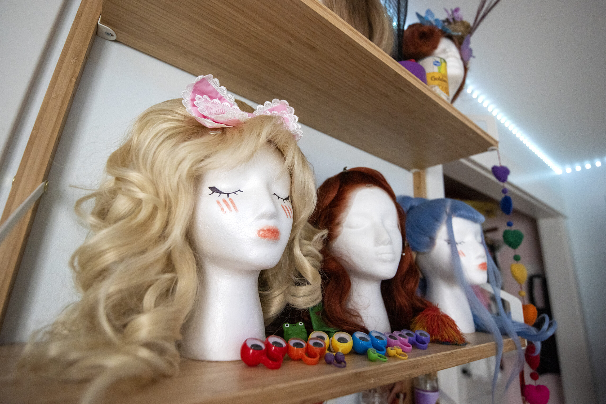 Wigs are on mannequin heads on a shelf.