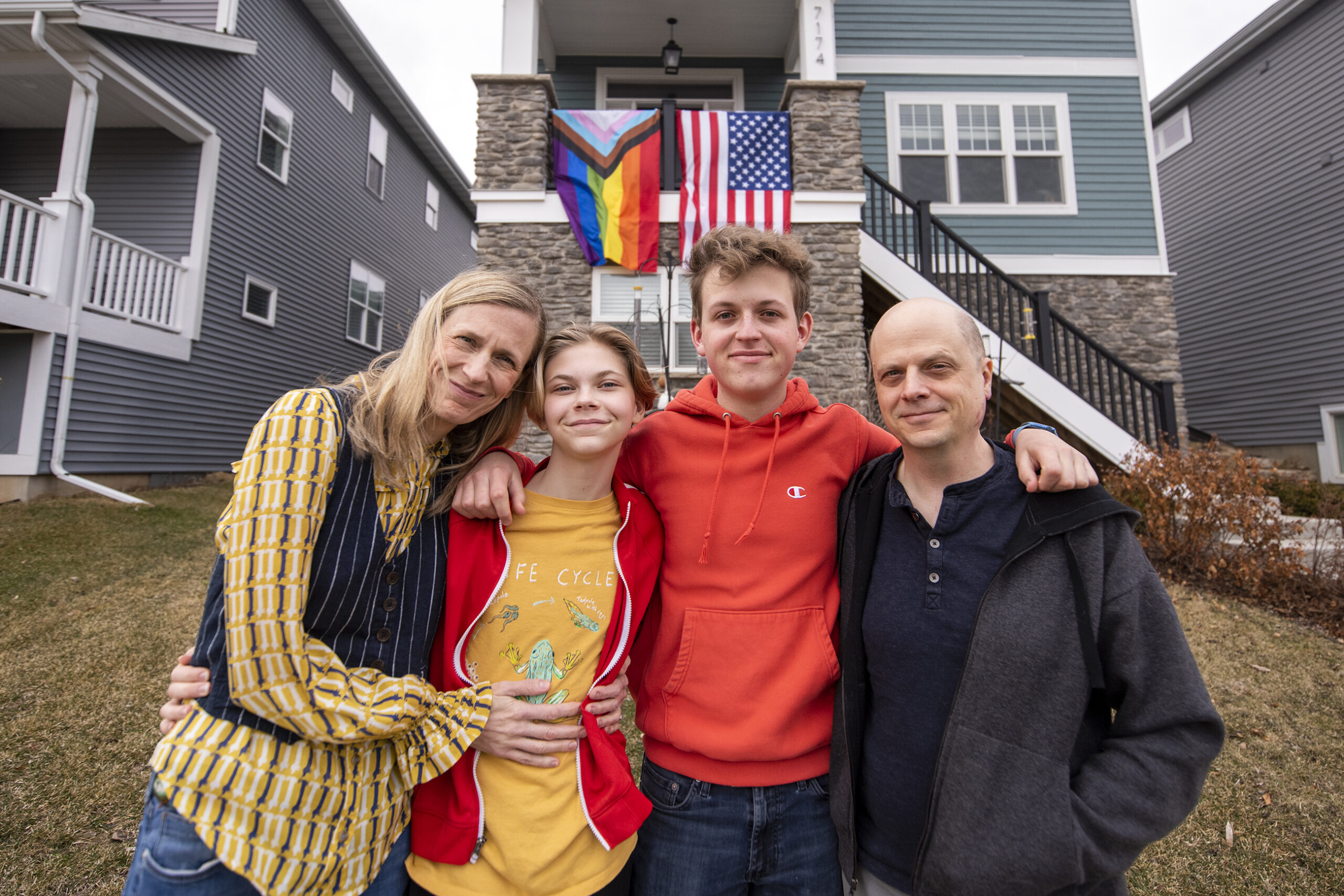 Bailey Mosling's family stands next to him outside of their home. An LGBT pride flag & U.S. flag hang outside their balcony.