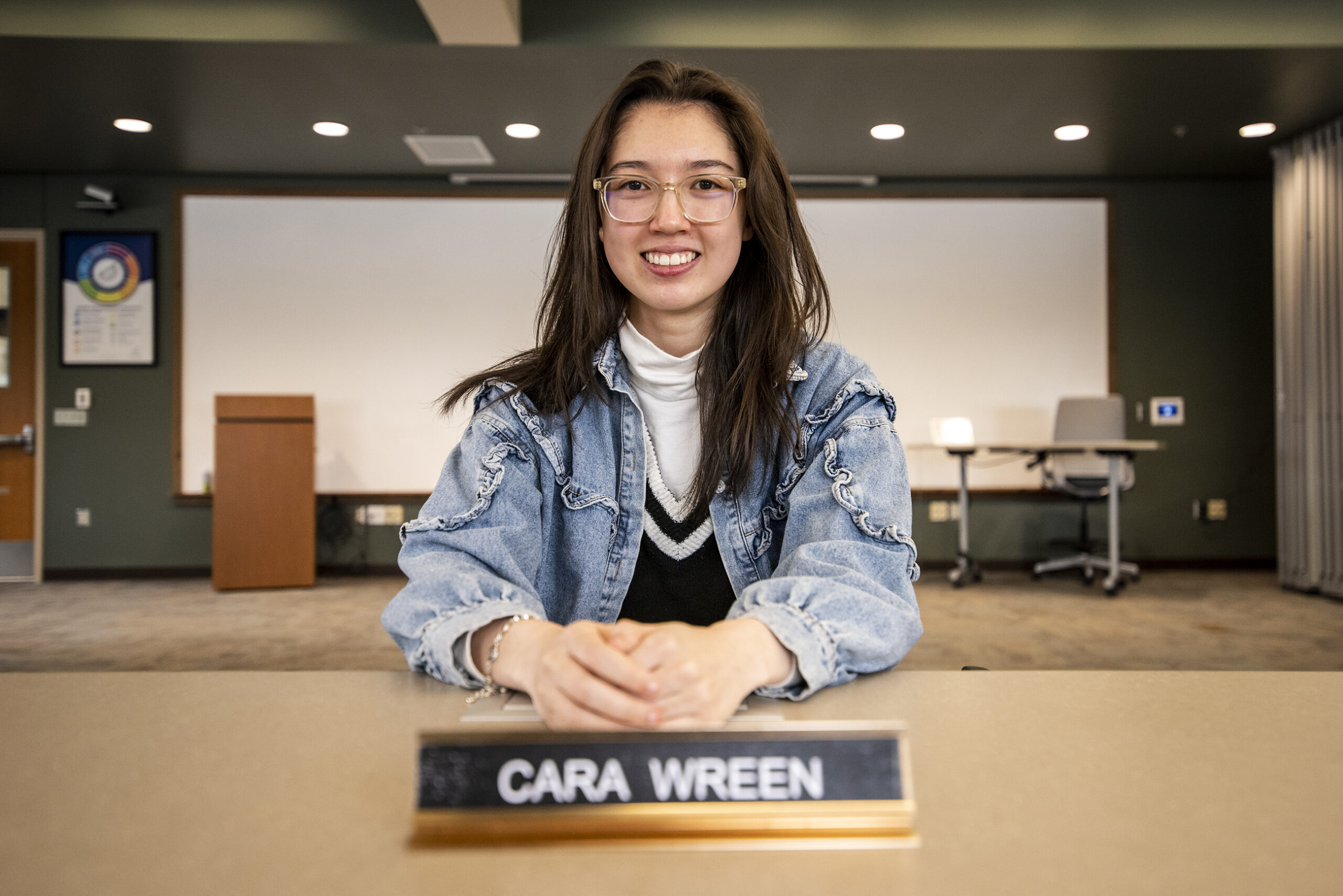 A student sits at a table in a conference room with a name plate.