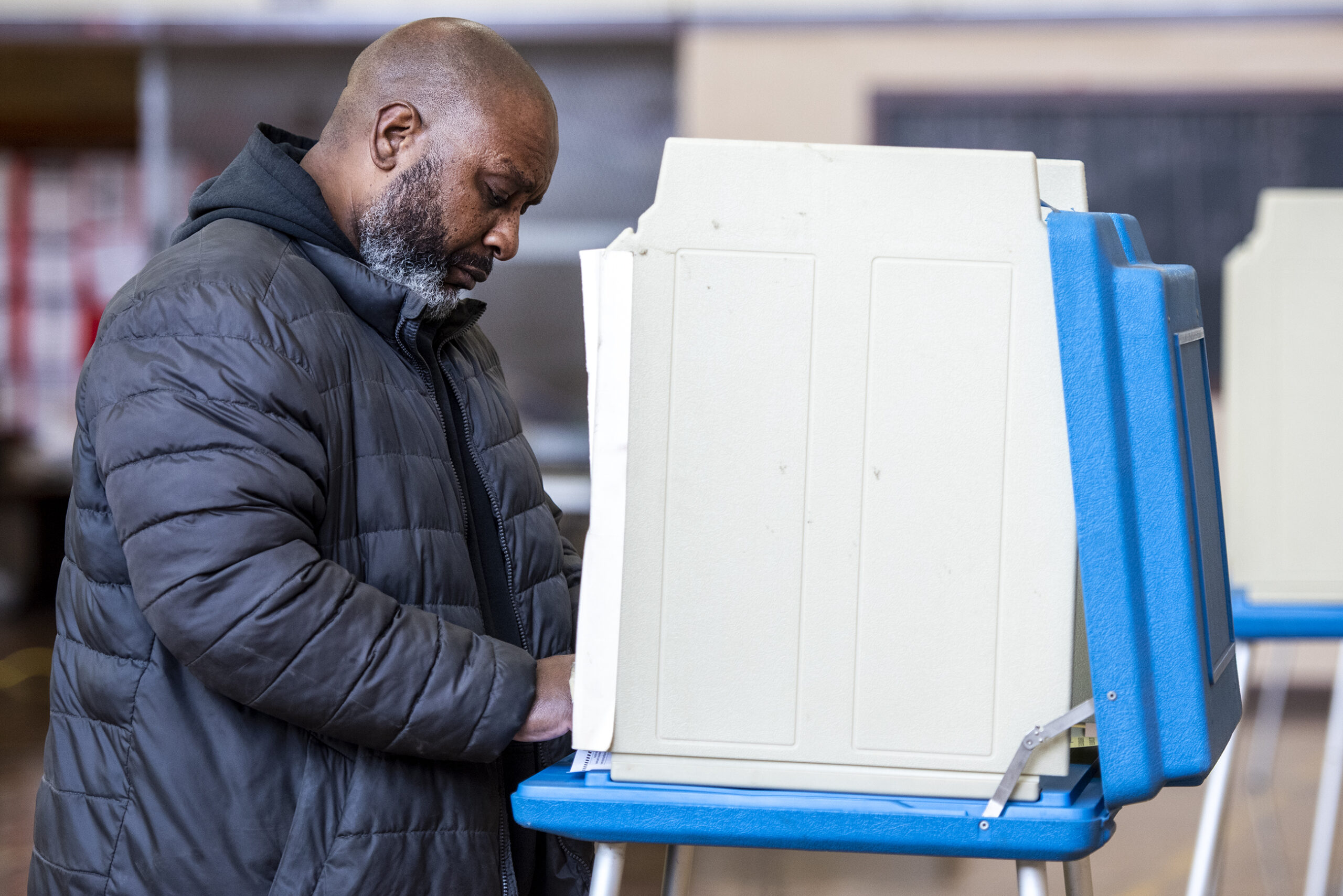 A voter in a jacket fills out a ballot at a voting booth.