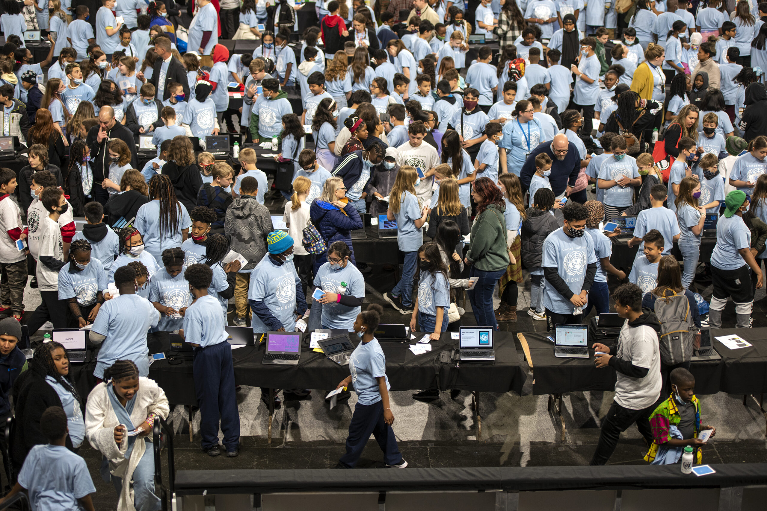 A crowd of students seen from above walk near black tables.