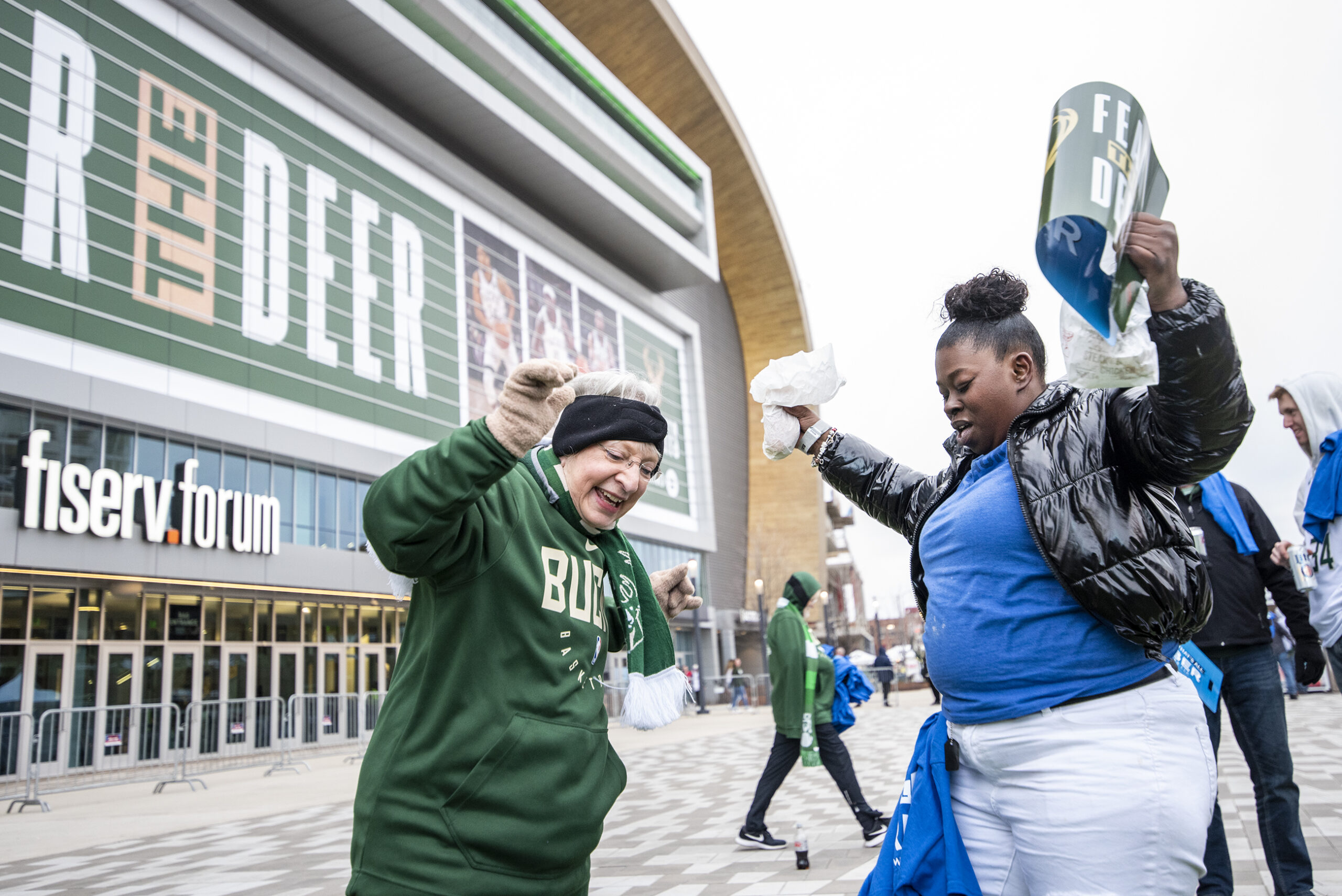 Two women raise their arms as they dance outside the Fiserv Forum.