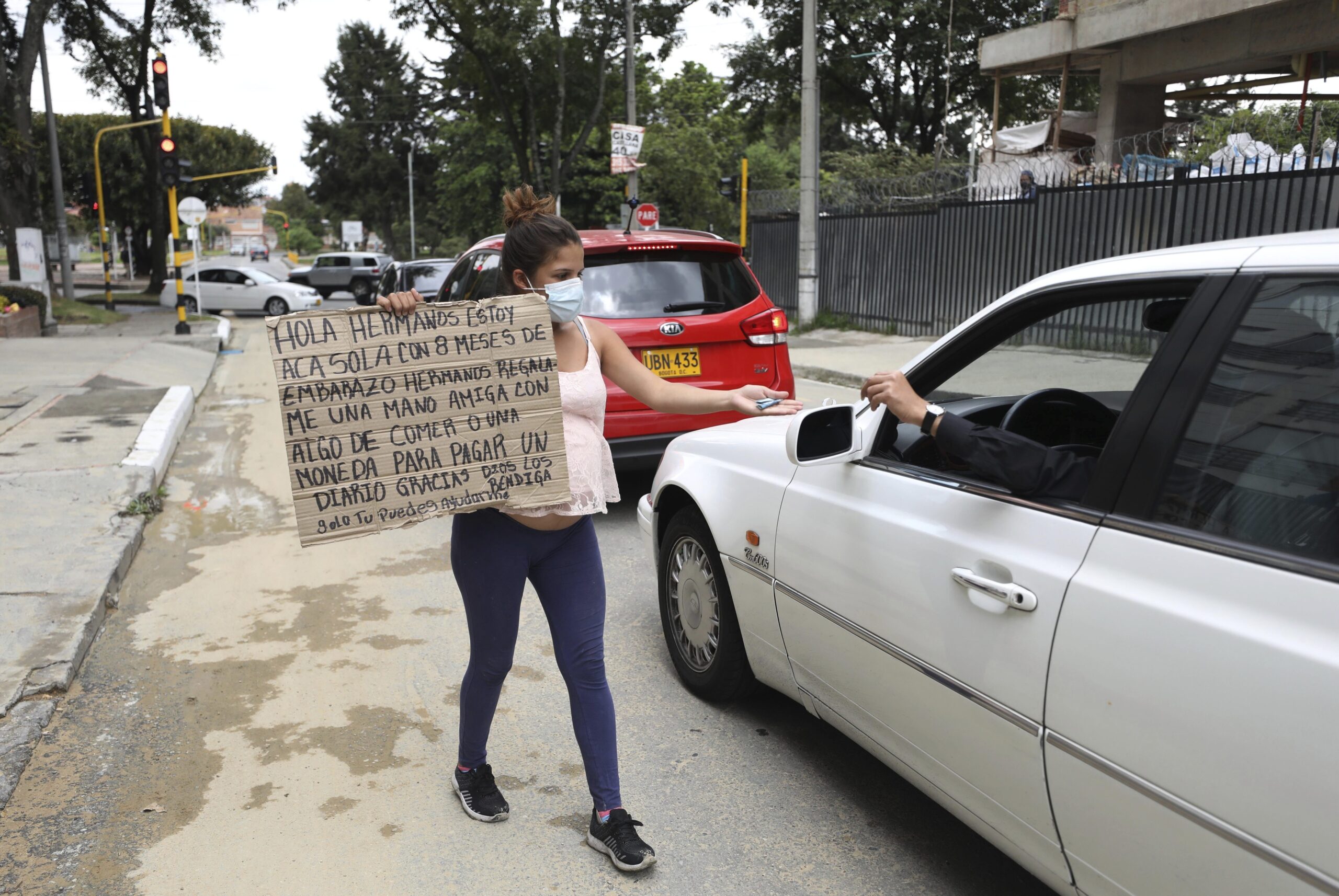 A pregnent woman holds a sign asking for food or money and reaches toward a car
