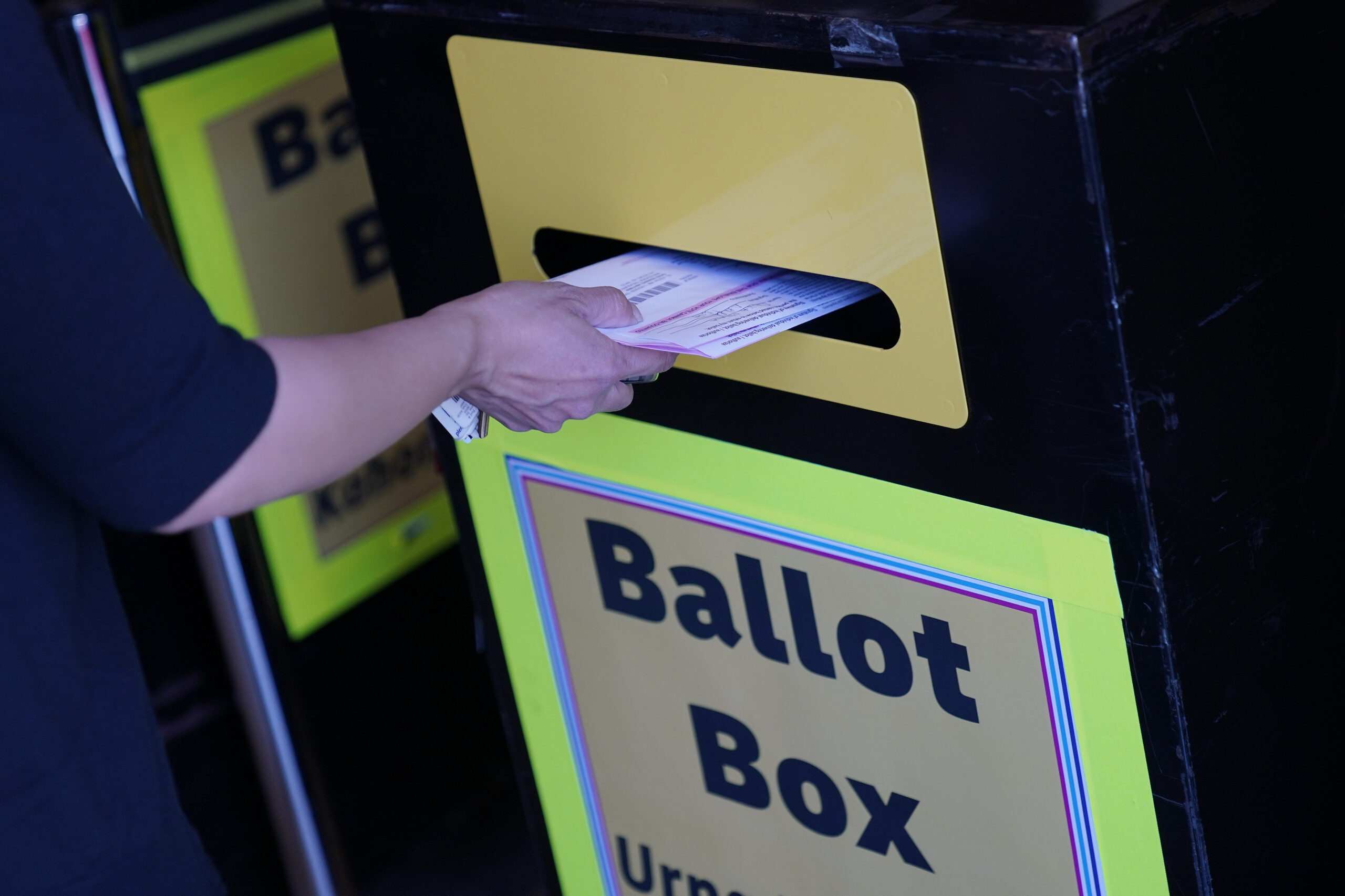 a person places a mail-in ballot in a drop box