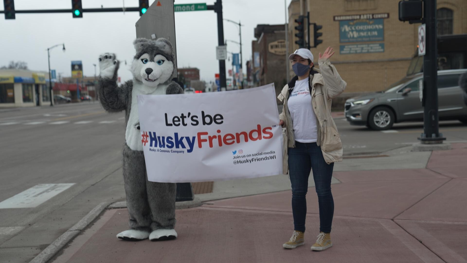A person dressed as a Husky and a woman walk holding a sign that says, "Let's be #HuskyFriends"