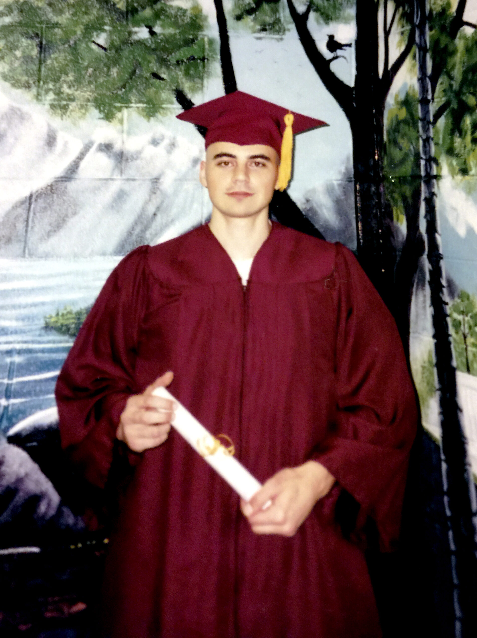 Jonathan Liebzeit in a cap and gown, holding his high school diploma
