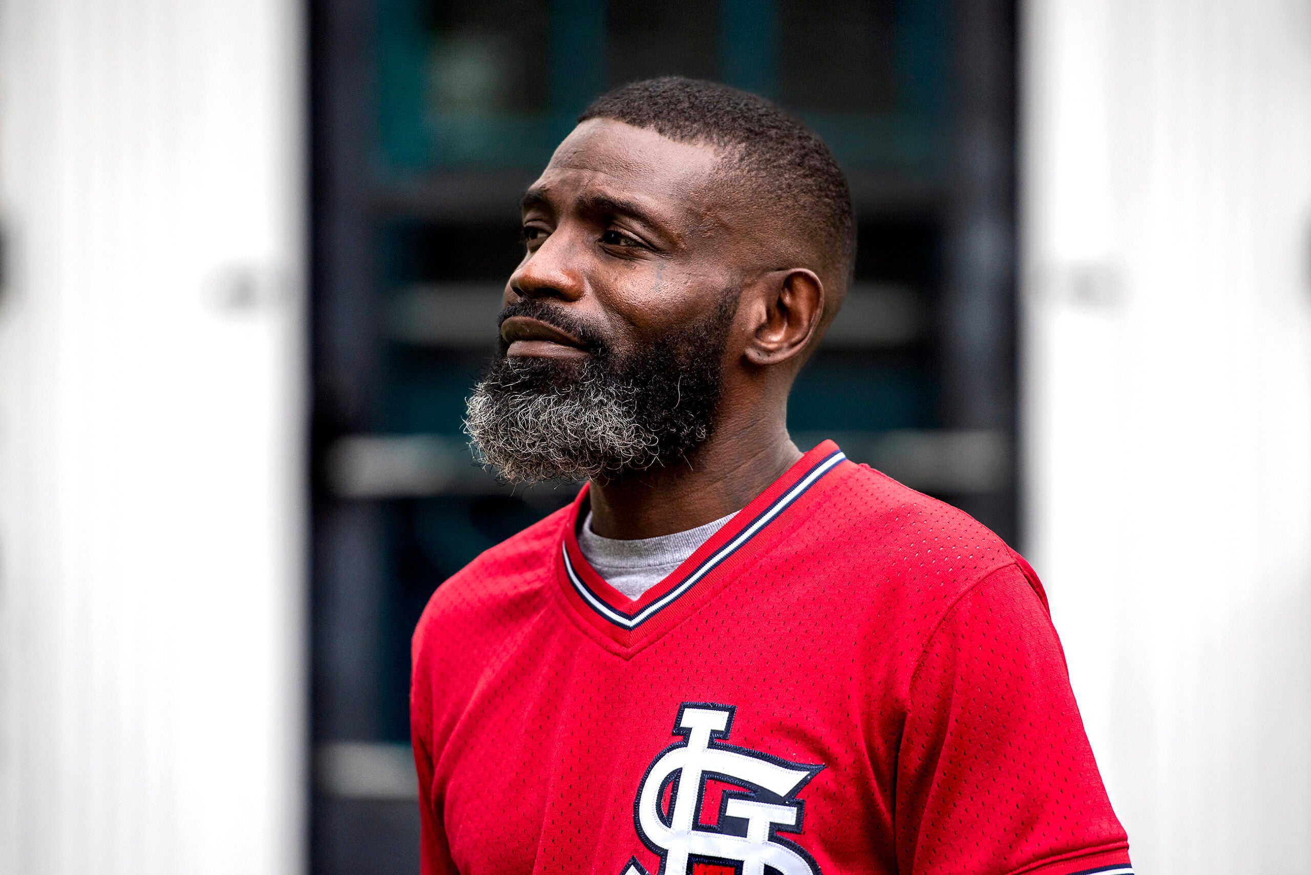 Segdrick Farley looks to the side as he stands in front of a dark door in a red shirt.