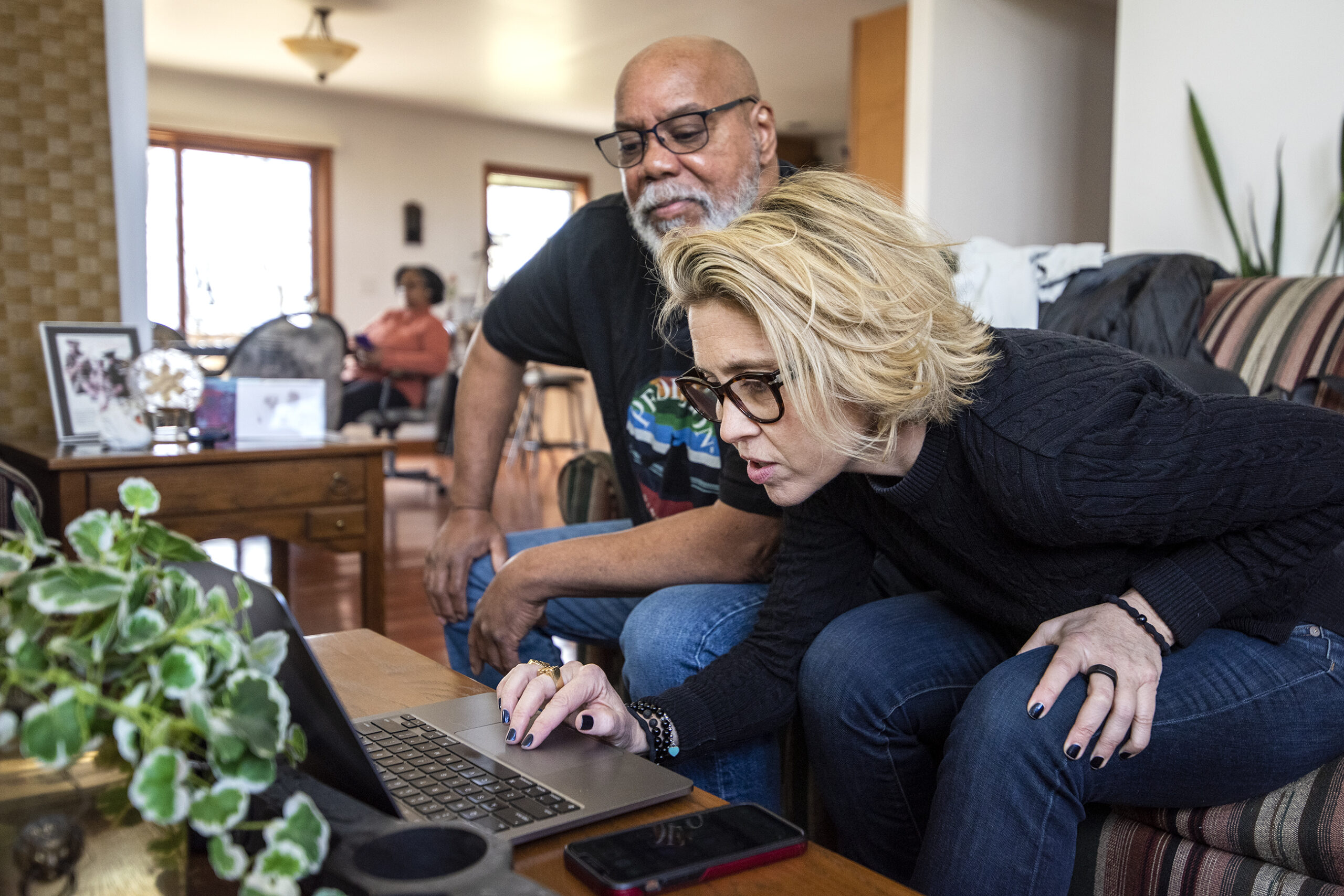 A woman and a man sit on a couch and look at photos on a laptop.