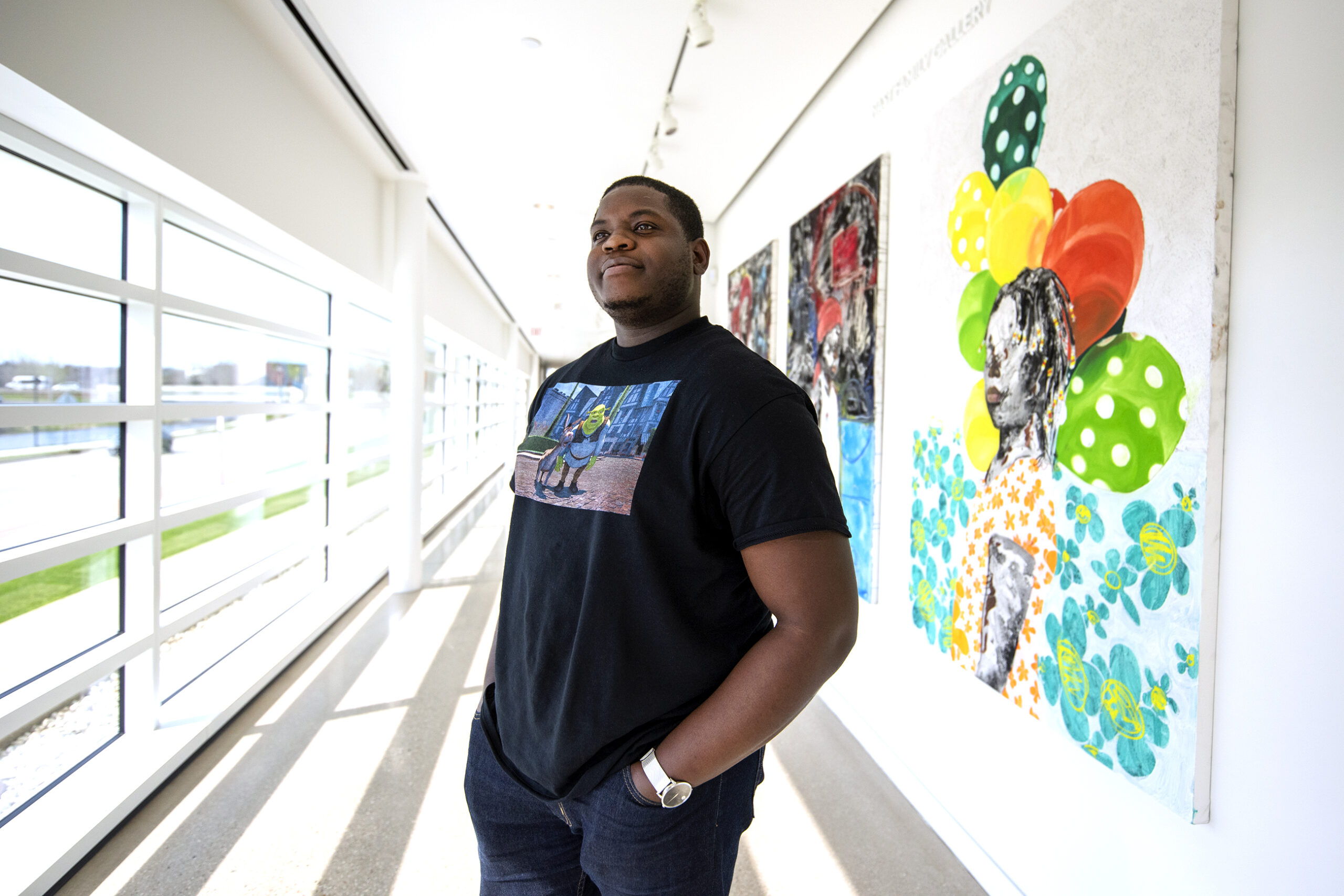 Khari Turner stands in a hallway with windows and colorful artwork displayed on the wall behind him.