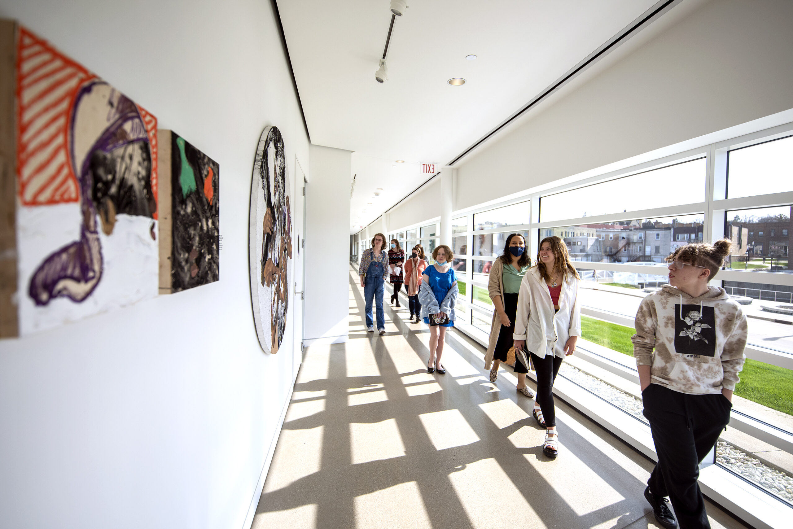 Teenagers walk in a line as they pass by works of art.