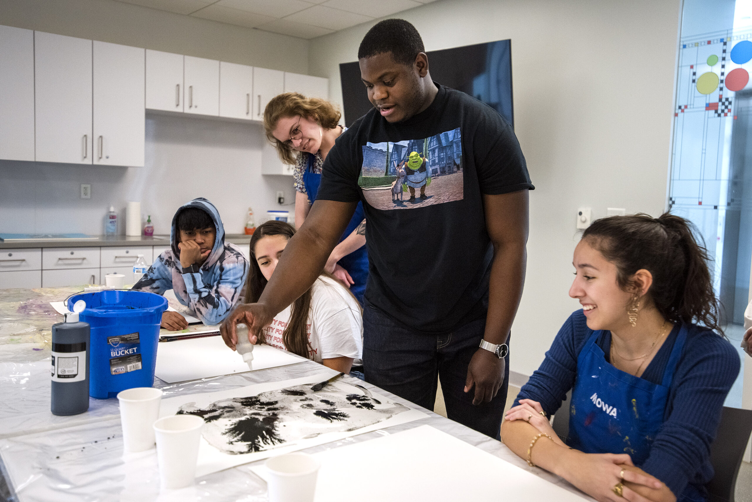 Teenagers smile as they watch Khari Turner use water from the Milwaukee River to mix with ink.