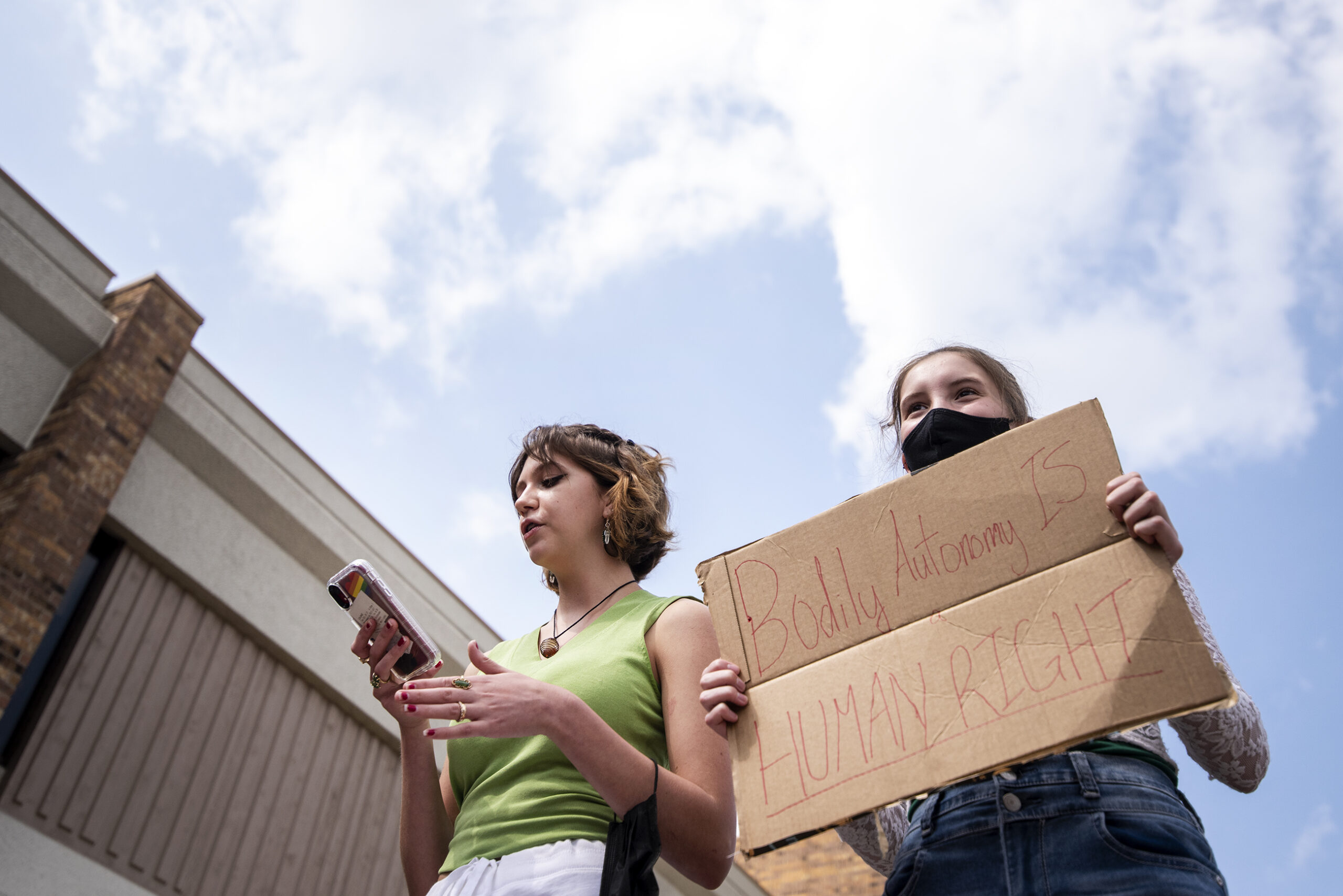 The sky can be seen behind two students as they speak during a walkout. One student holds a sign that says 