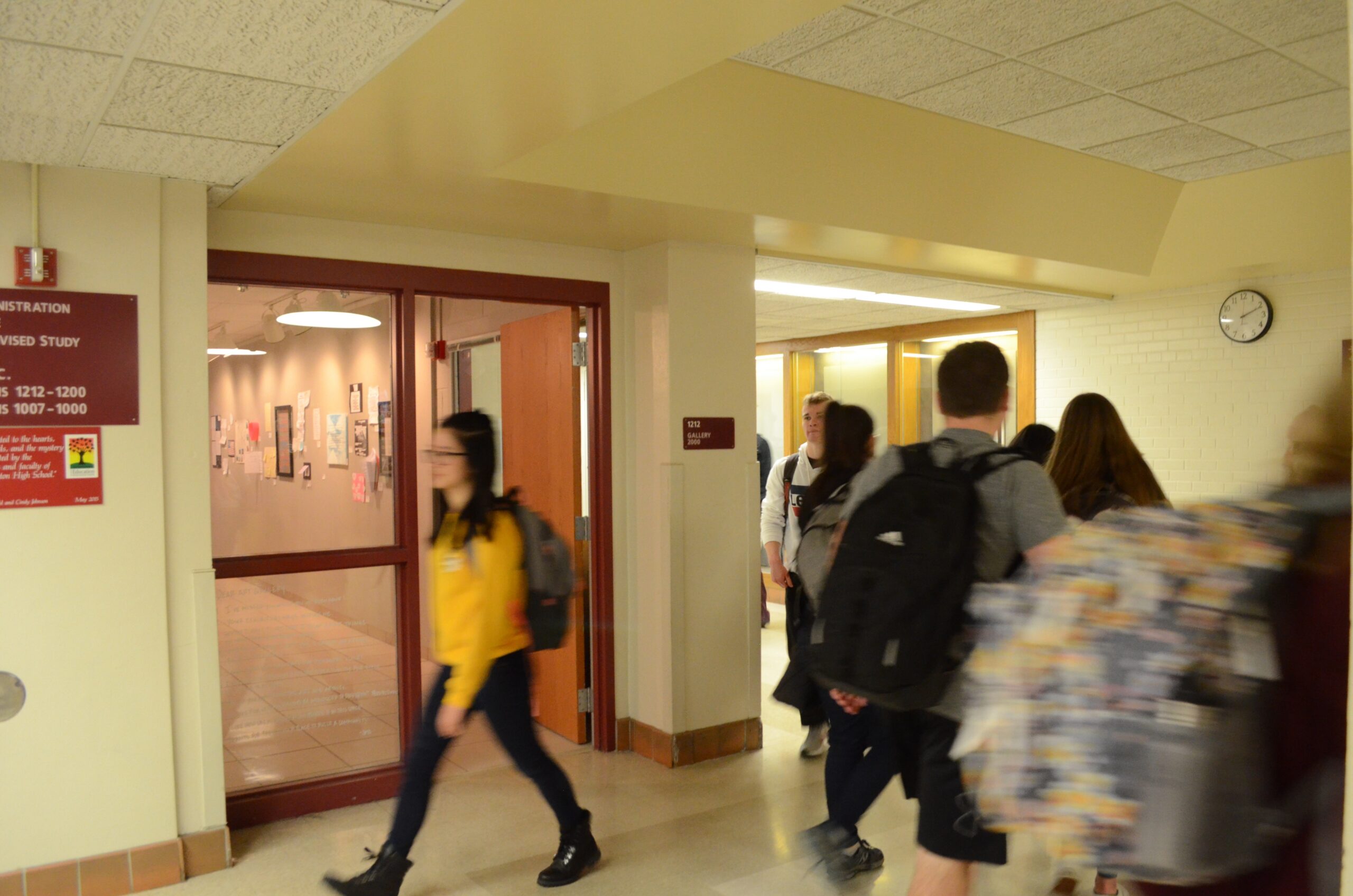 Students carrying backpacks, blurred with motion, walk through the red-and-white hallways of Middleton High School.
