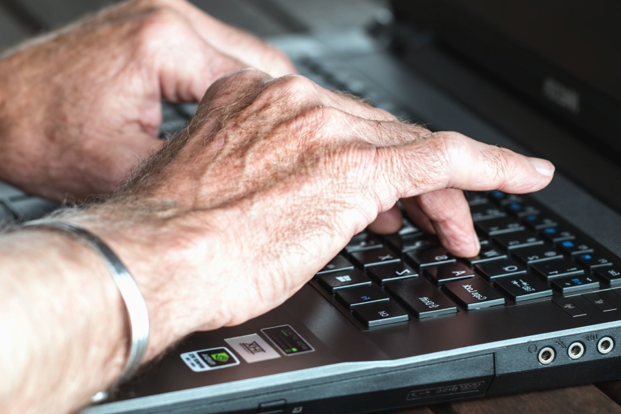 An older person types on a laptop.