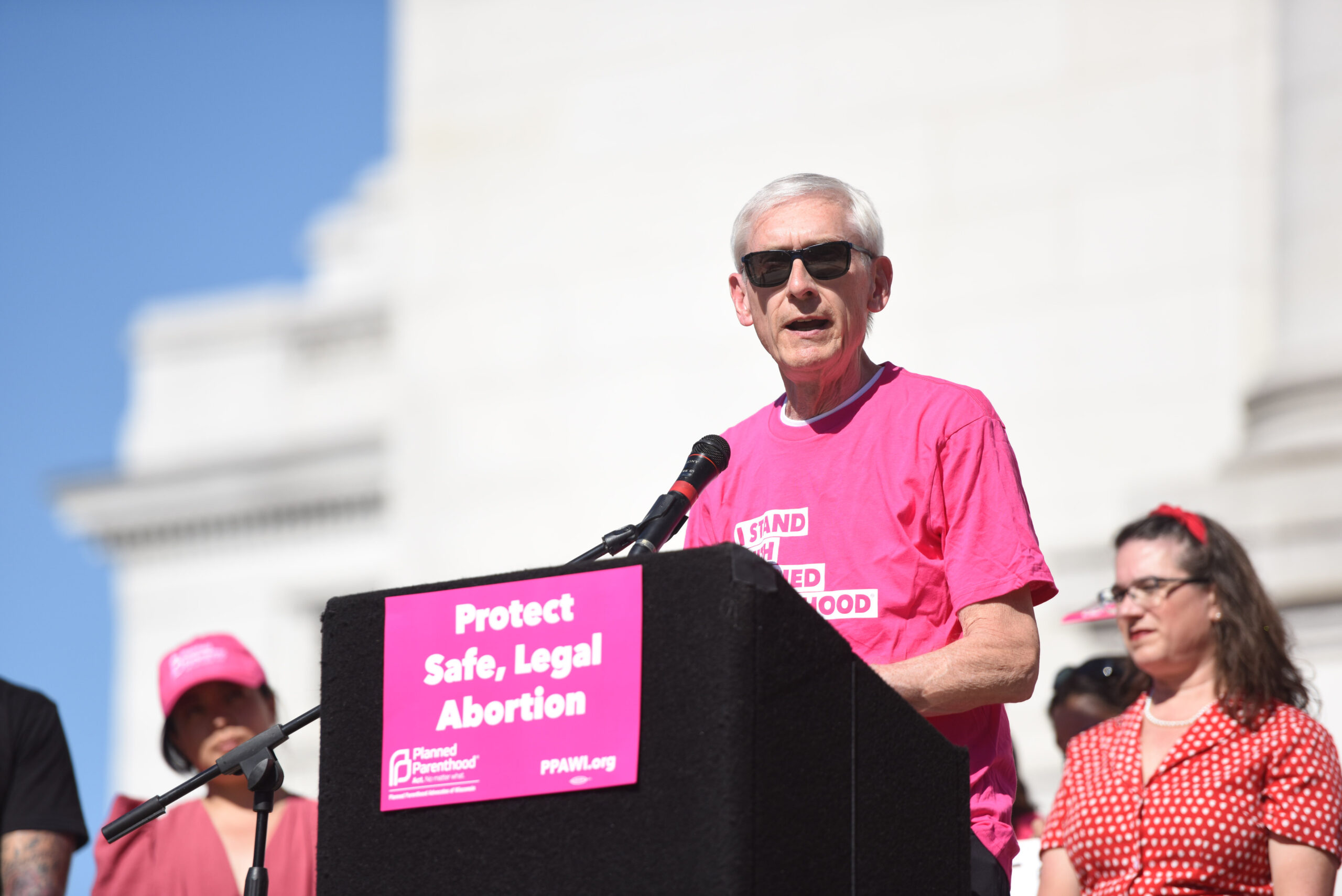 Gov. Tony Evers wears a pink Planned Parenthood shirt while speaking outside at a protest.