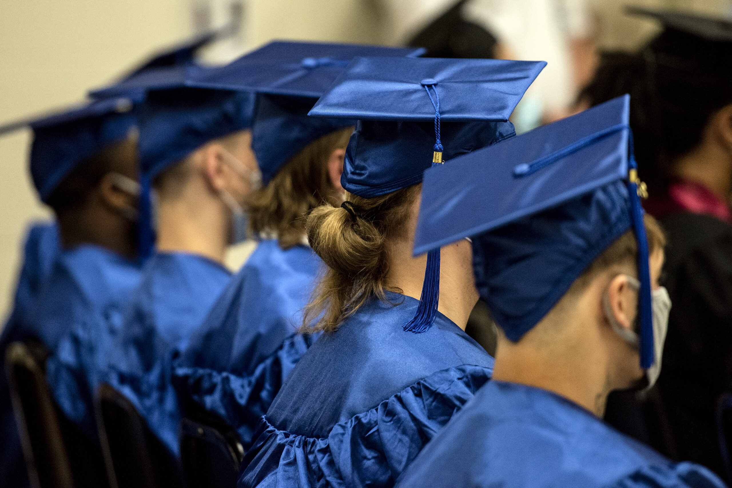 Blue graduation caps can be seen in a line as graduates sit together.