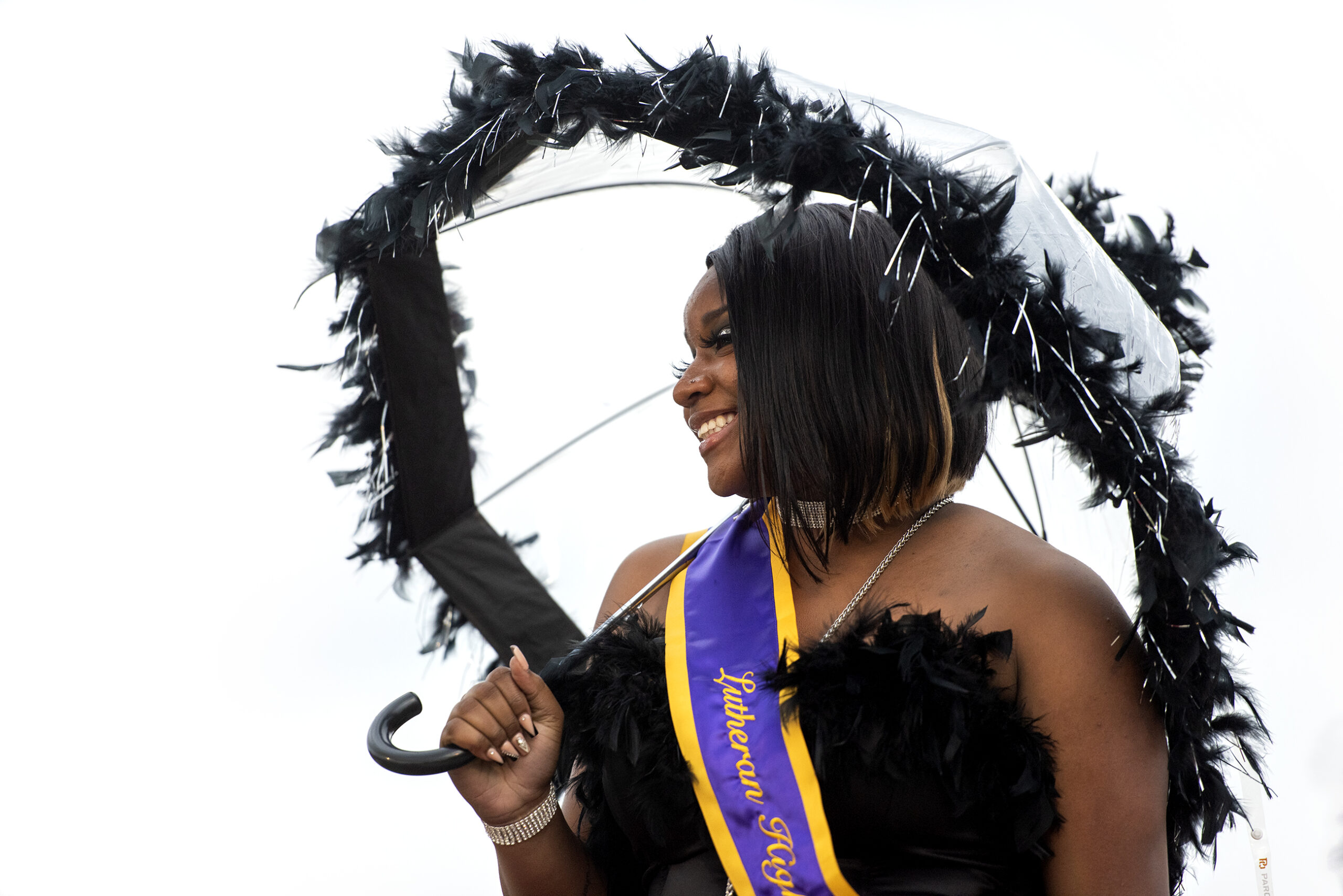 An attendee wears a black dress and holds a matching parasol as she smiles for a photo.
