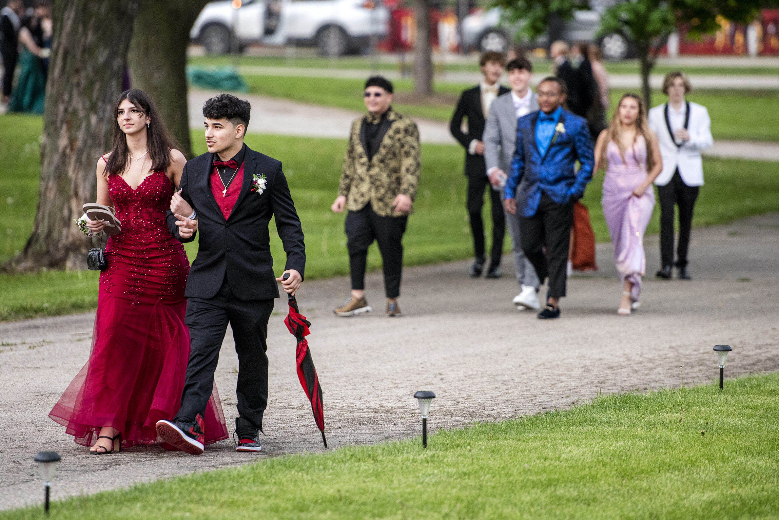 A girl in a dark red gown walks with a boy in a black suit with matching red details.