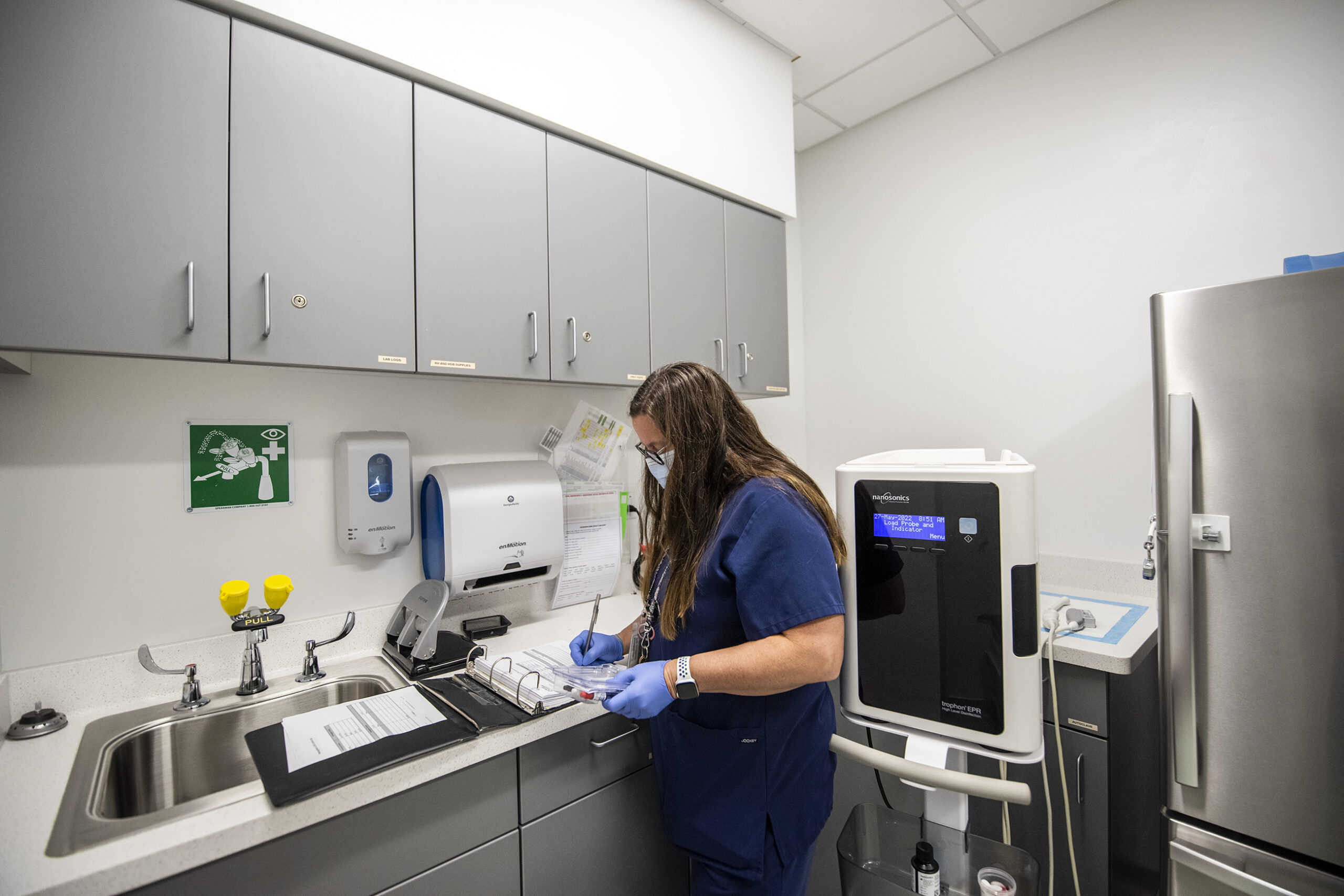 A nurse works in a clinic room with white walls and medical equipment.