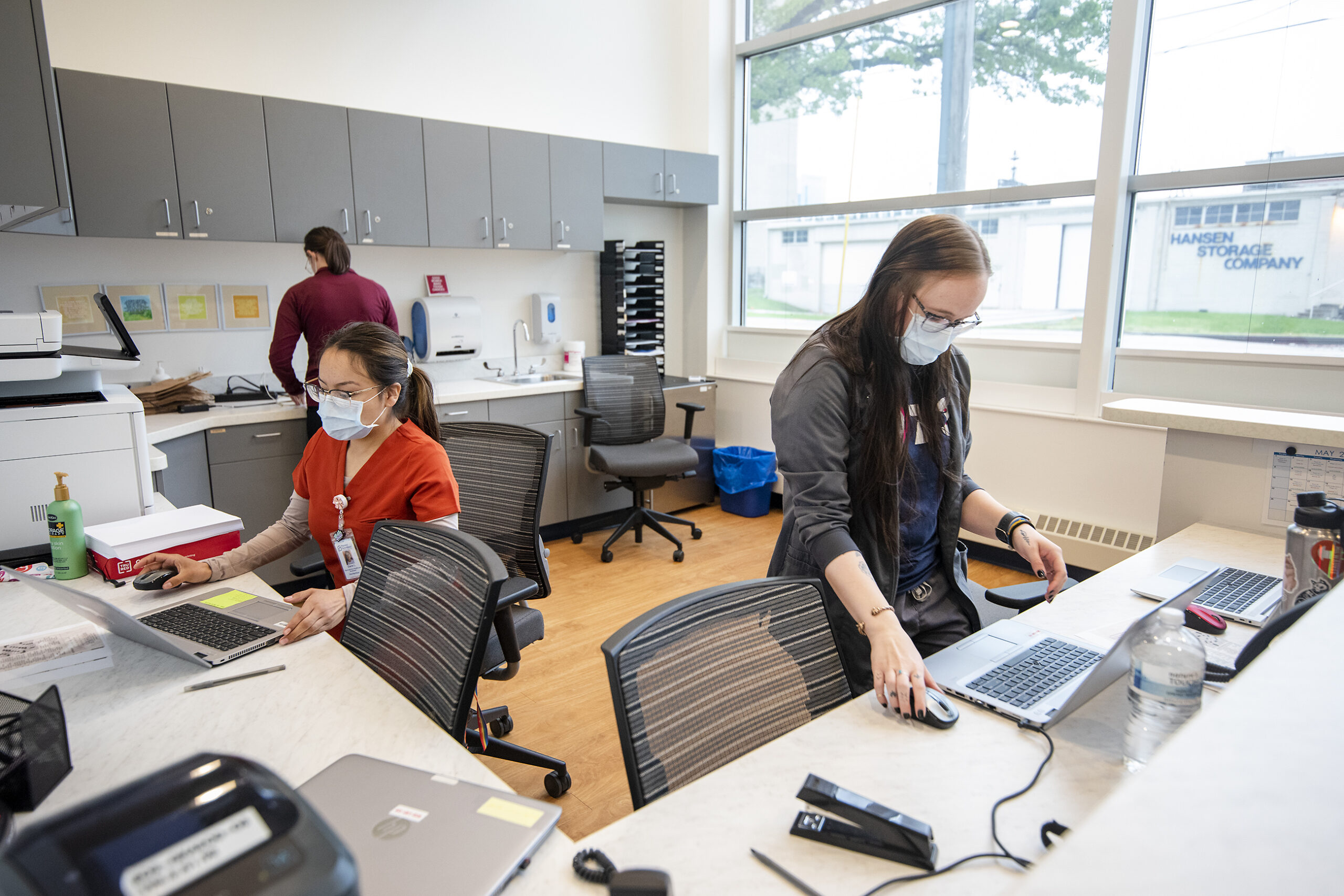 Several nurses work on computers at a wrap-around counter.