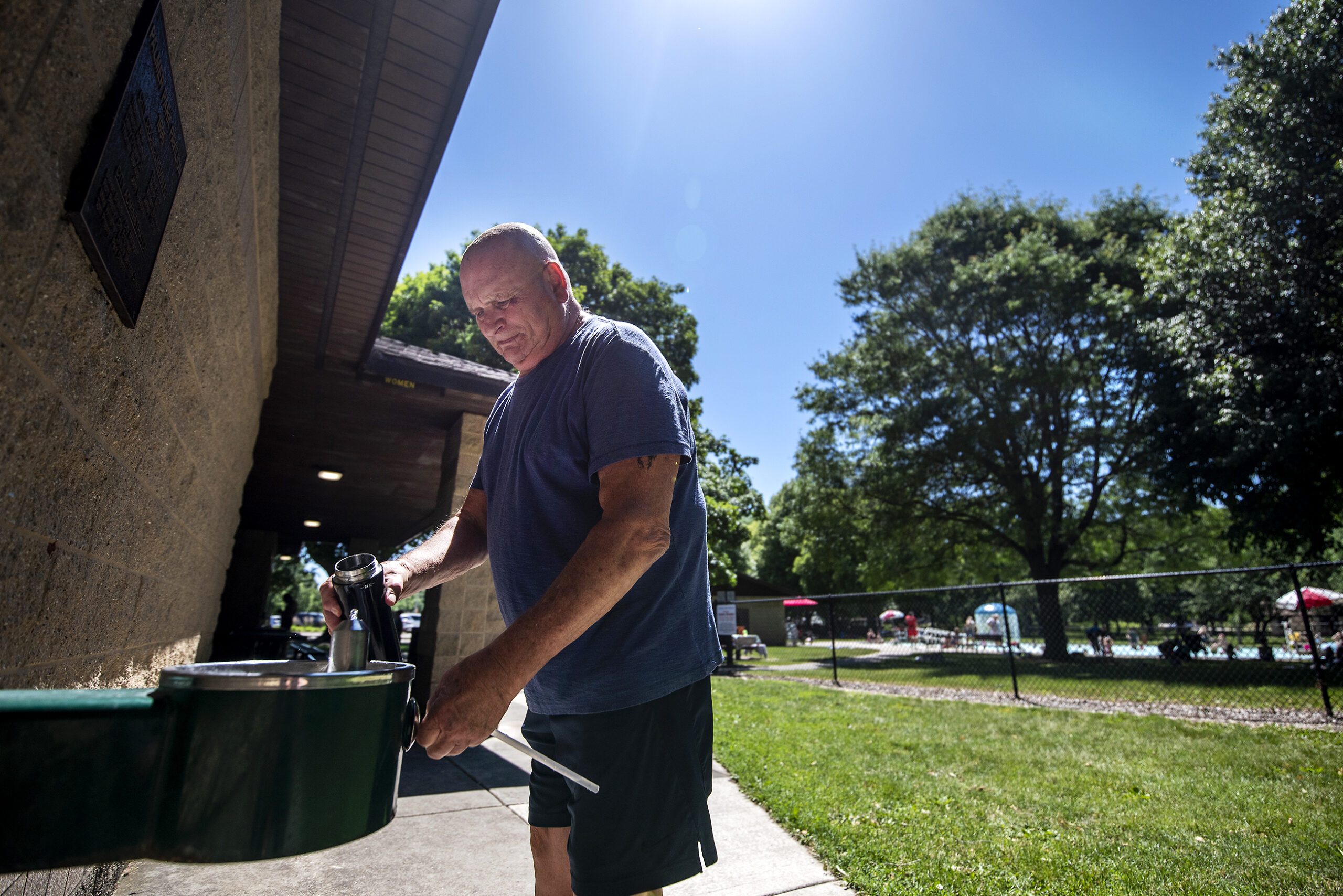 A man holds a water bottle up to an outdoor water fountain.