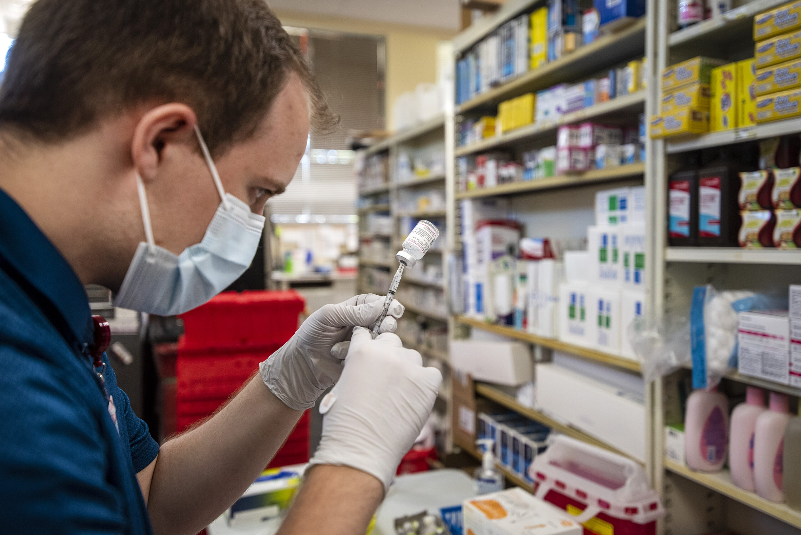 A vaccine is transferred from a vile to a syringe in the back of a pharmacy.