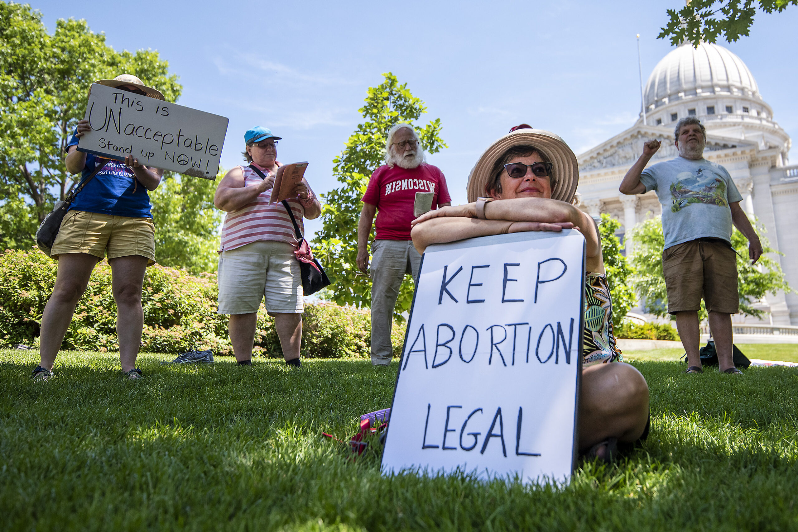 A woman looks upward as she holds a sign that says "Keep abortion legal." Singers stand behind her in a line.