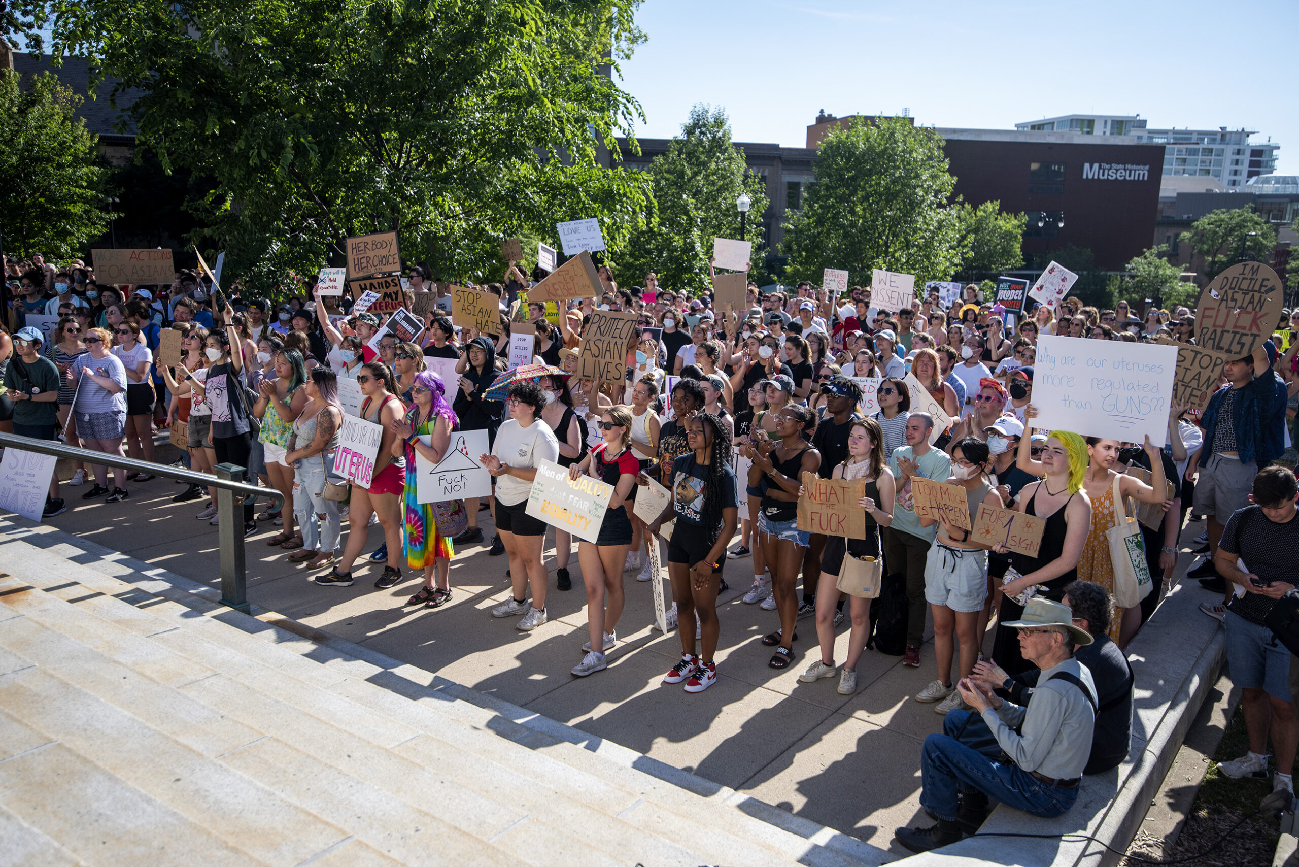 A crowd of protesters hold signs on the capitol steps.