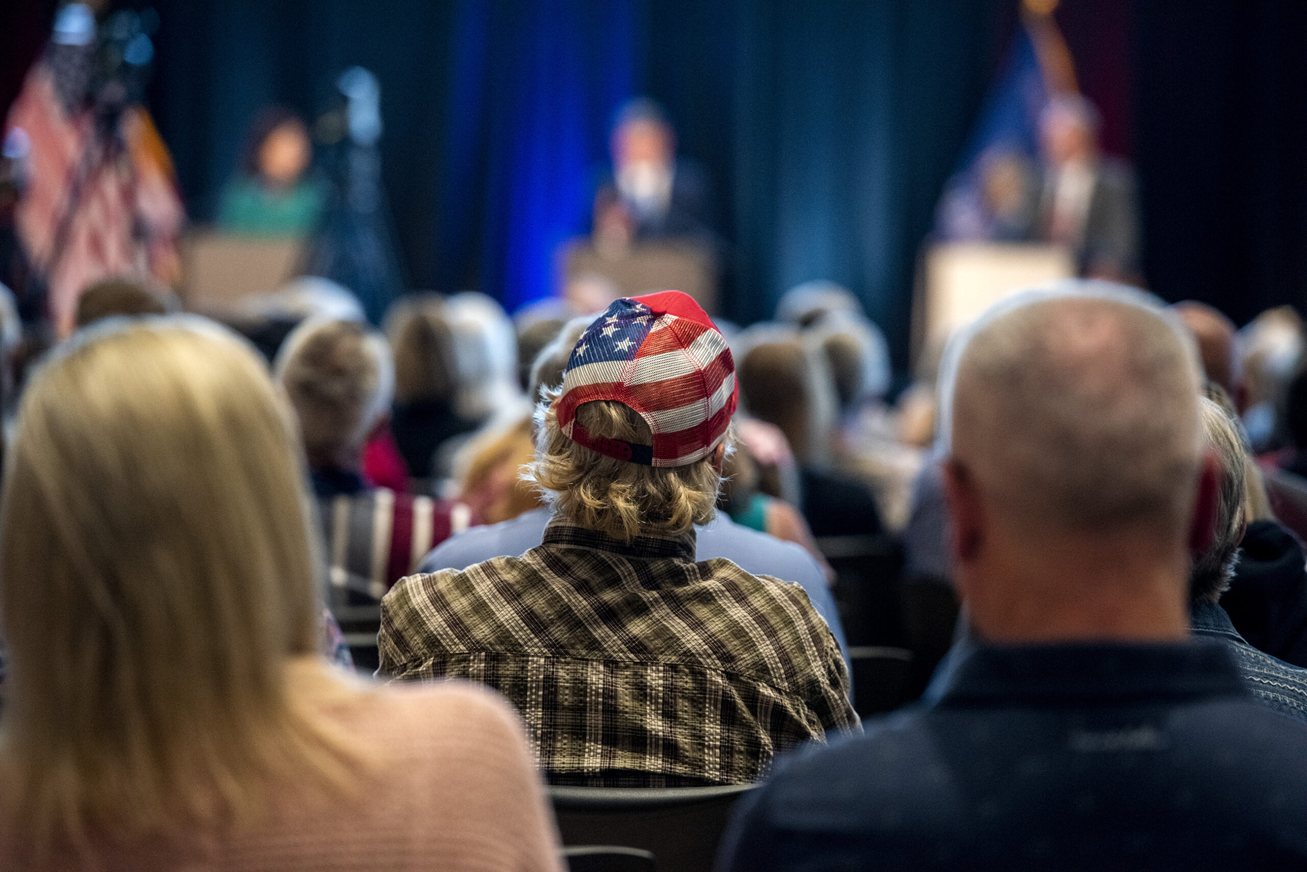 An attendee in a U.S. flag pattern hat sits in the crowd.