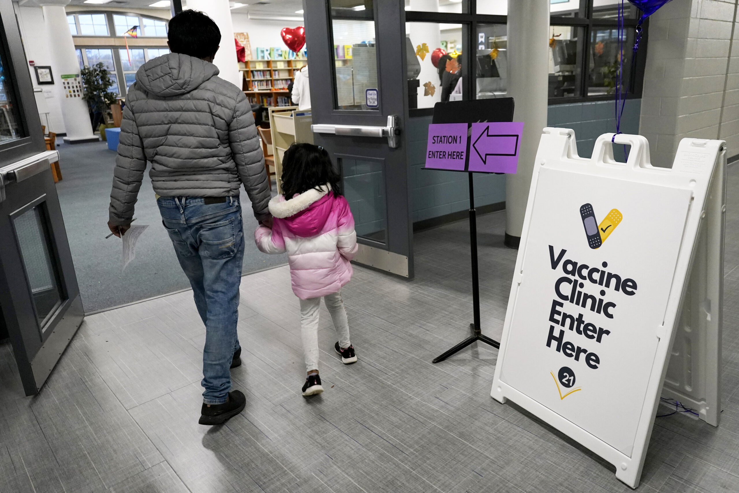 An information sign is displayed as a child arrives with her parent to receive the Pfizer COVID-19 vaccine