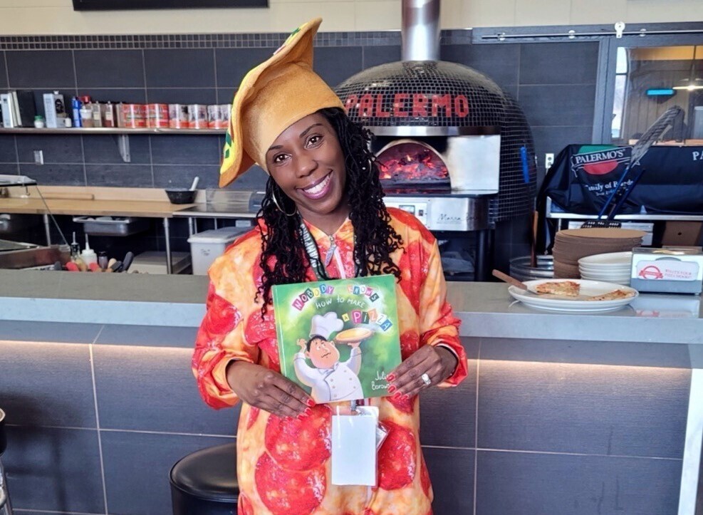 Dannette Justus holds a children's book while dressed in a pepperoni pizza costume