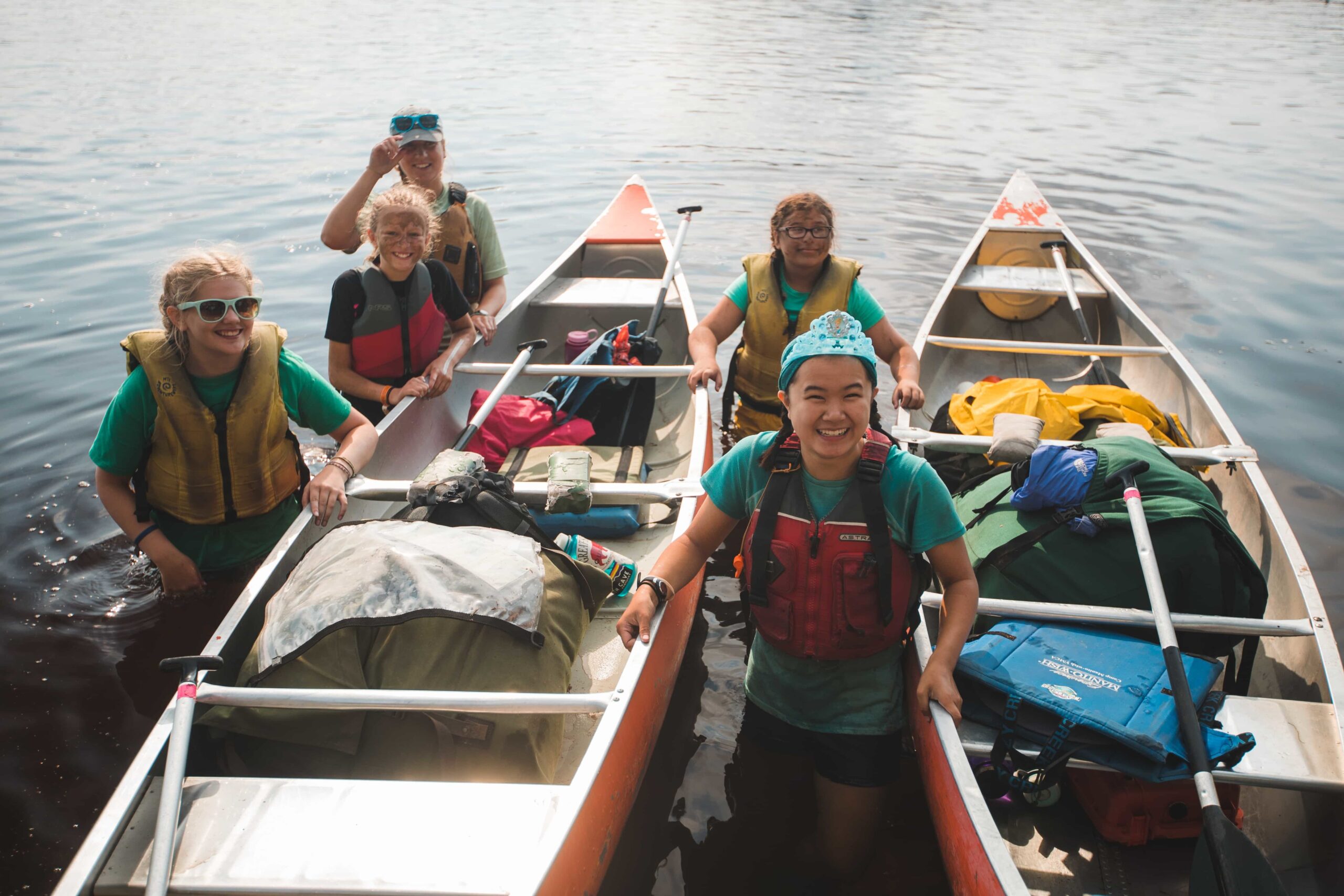 A group of camp-goers pose for a photo while standing alongside two canoes at Camp Manito-wish YMCA