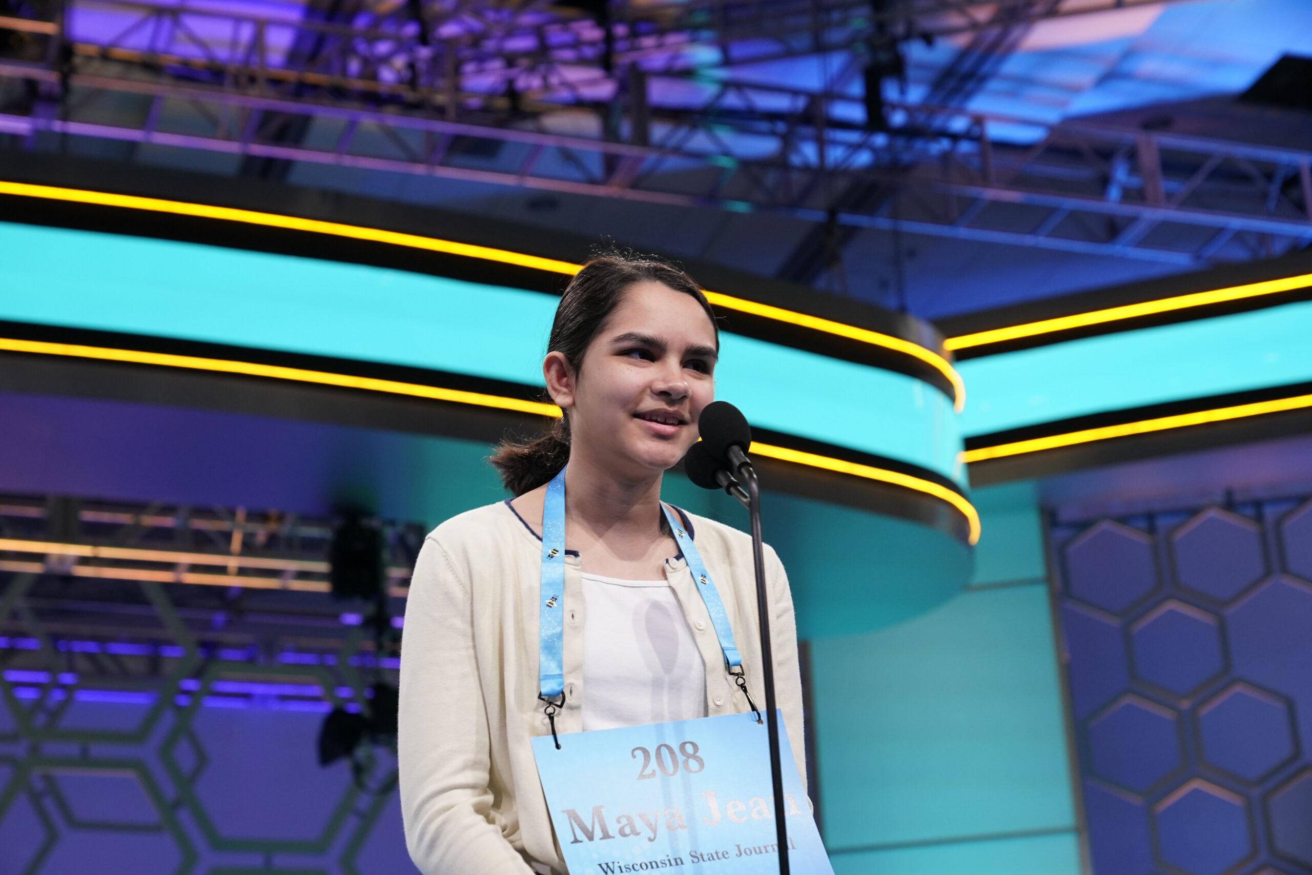 Maya Jadhav stands at a microphone on stage at the Scripps National Spelling Bee