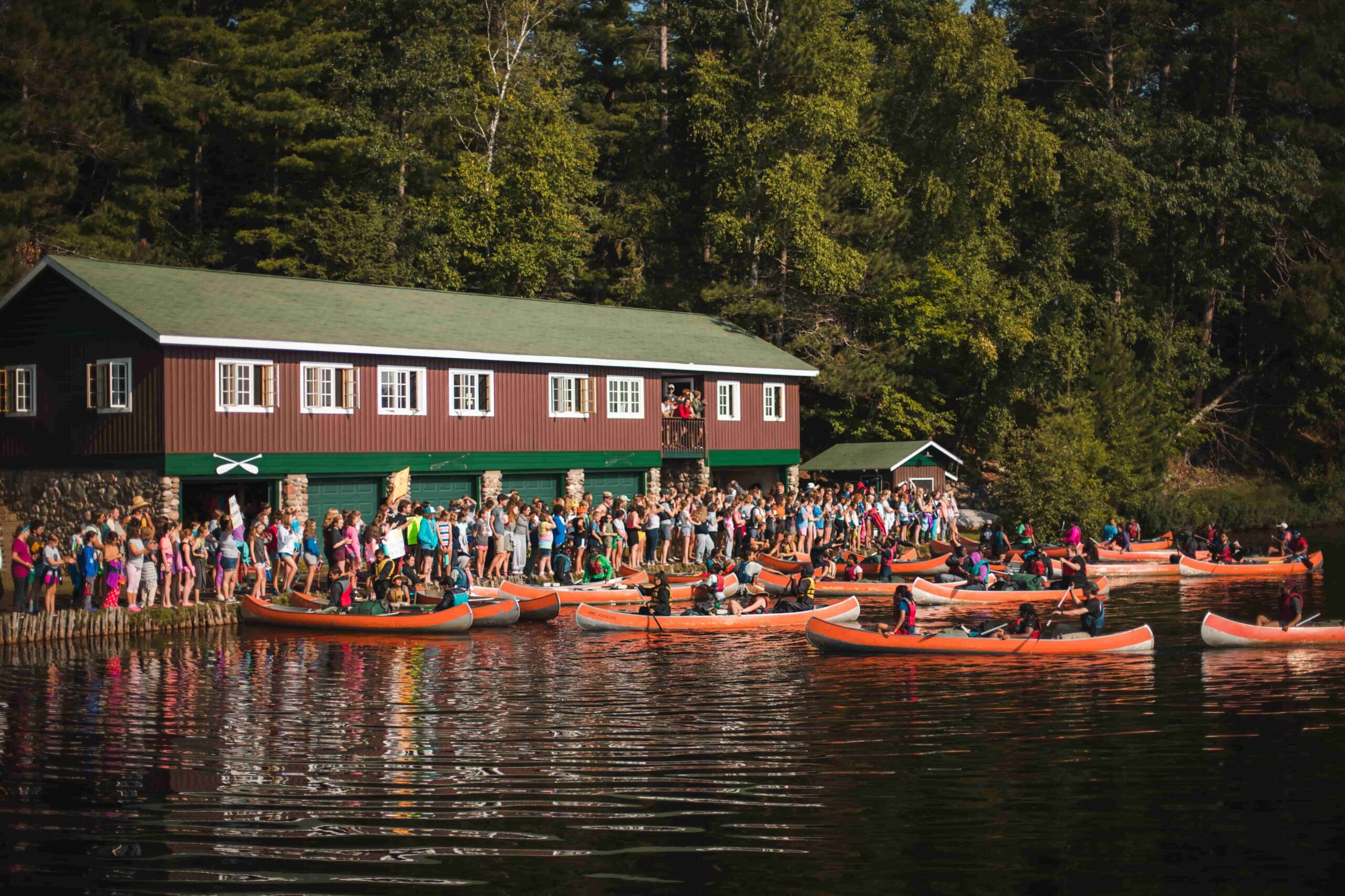 Camp Manito-wish YMCA counselors and campers lineup on the shore while others paddle canoes