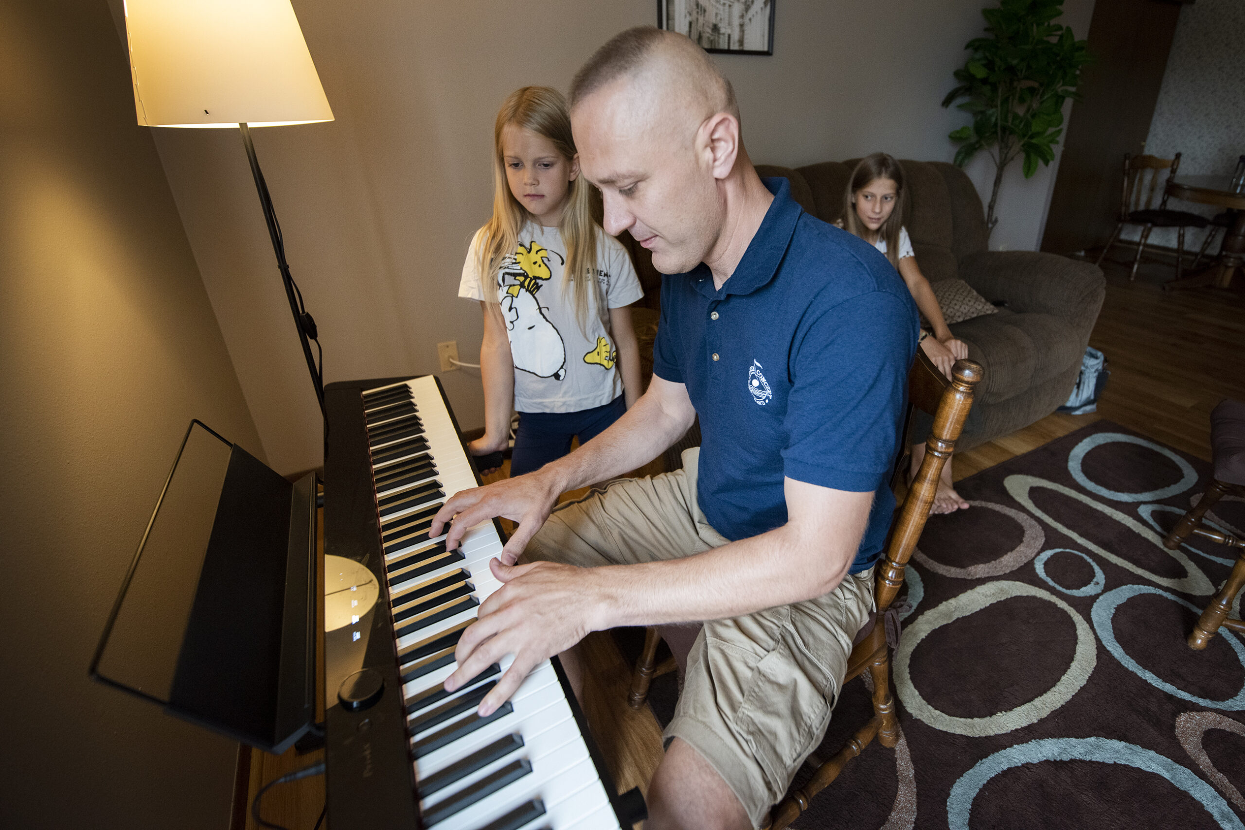 Peter Sokor plays a keyboard as his daughters watch.