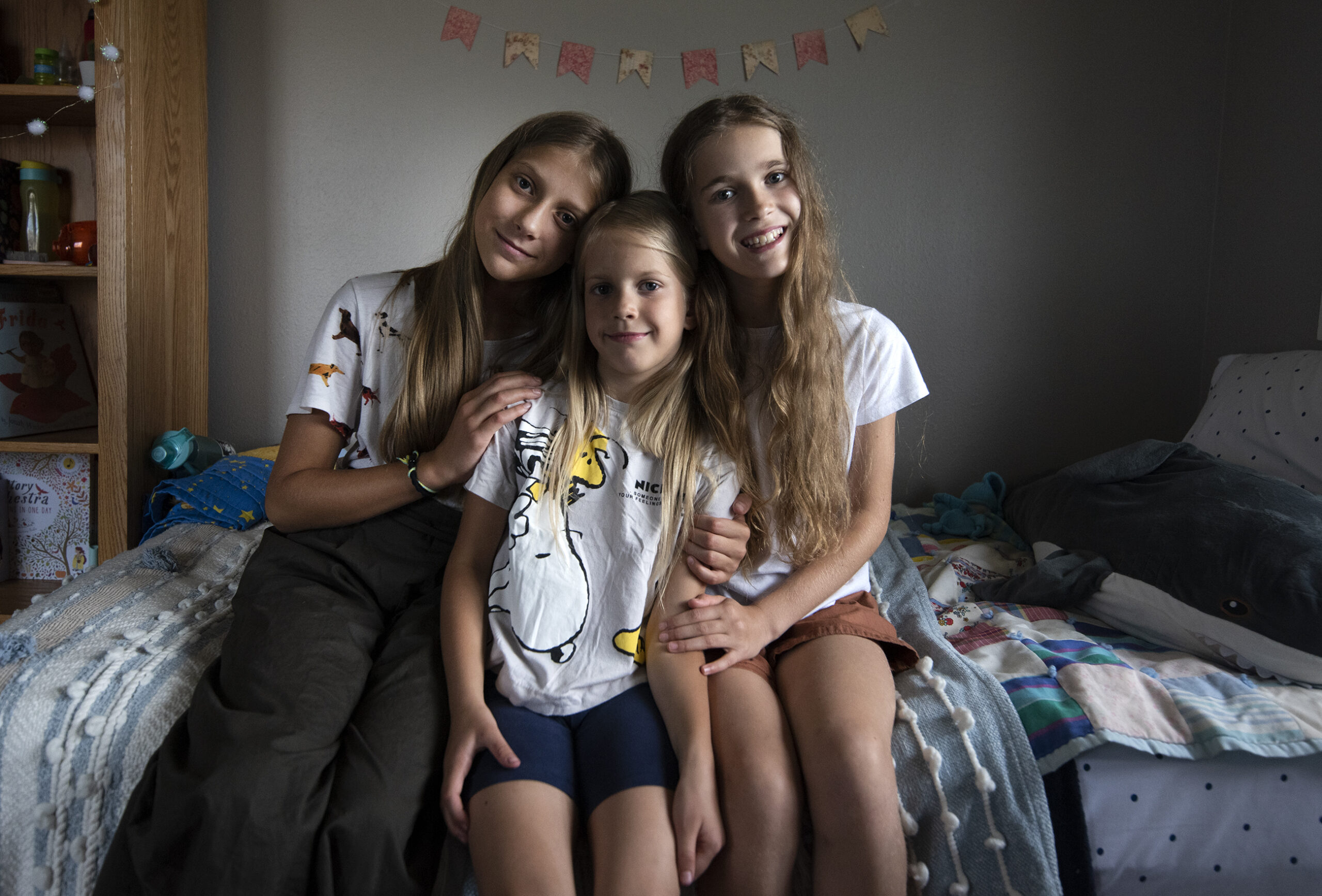 Three girls sit together on a bed.