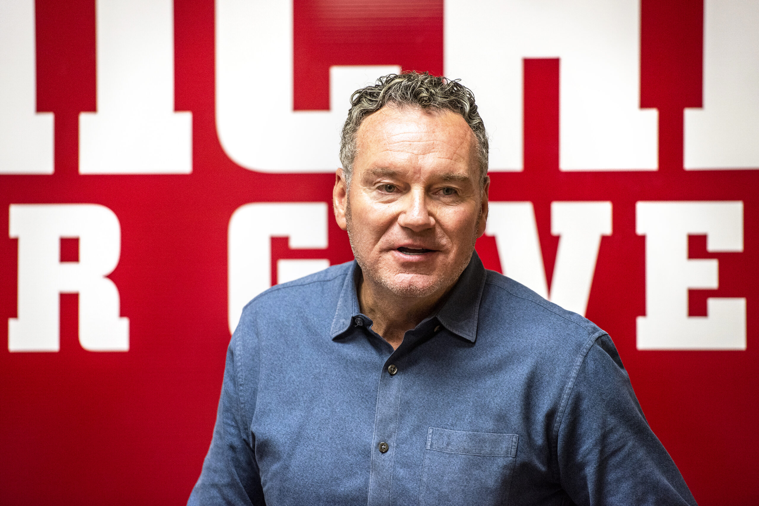 Tim Michels stands in front of a red banner as he speaks.