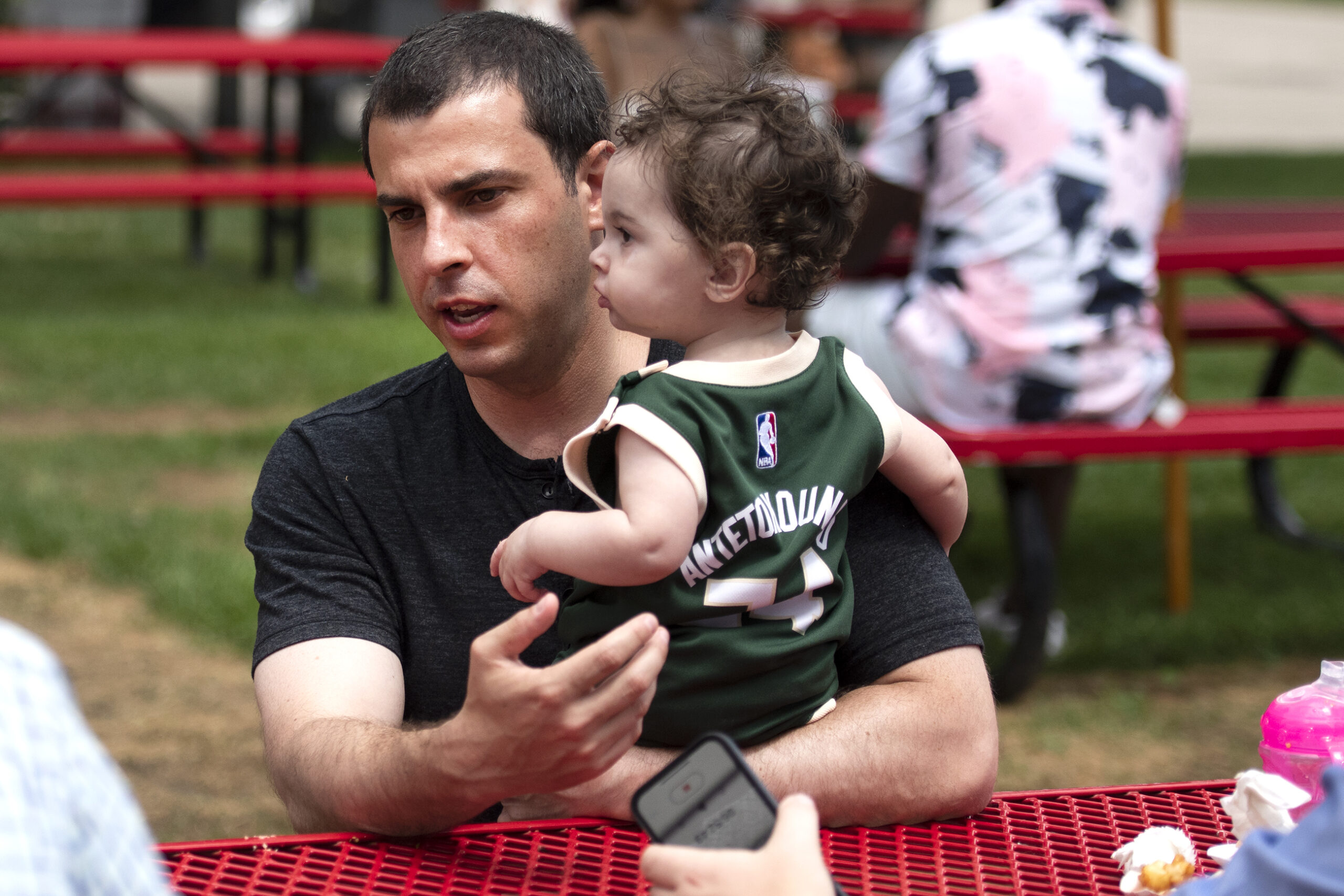 Alex Lasry sits at a picnic table as he holds his young daughter.