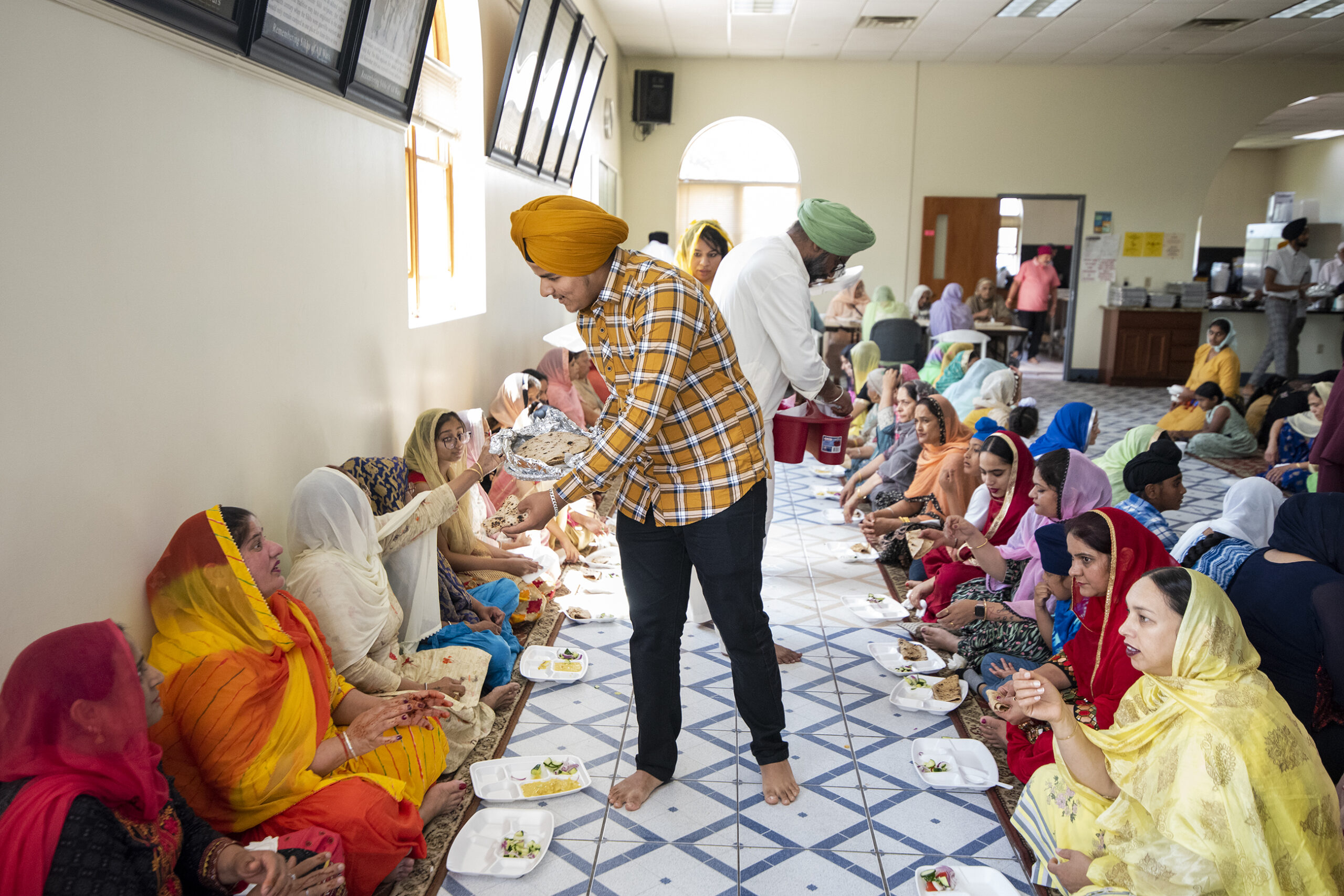A man serves temple members who sit on the ground together to enjoy a meal.
