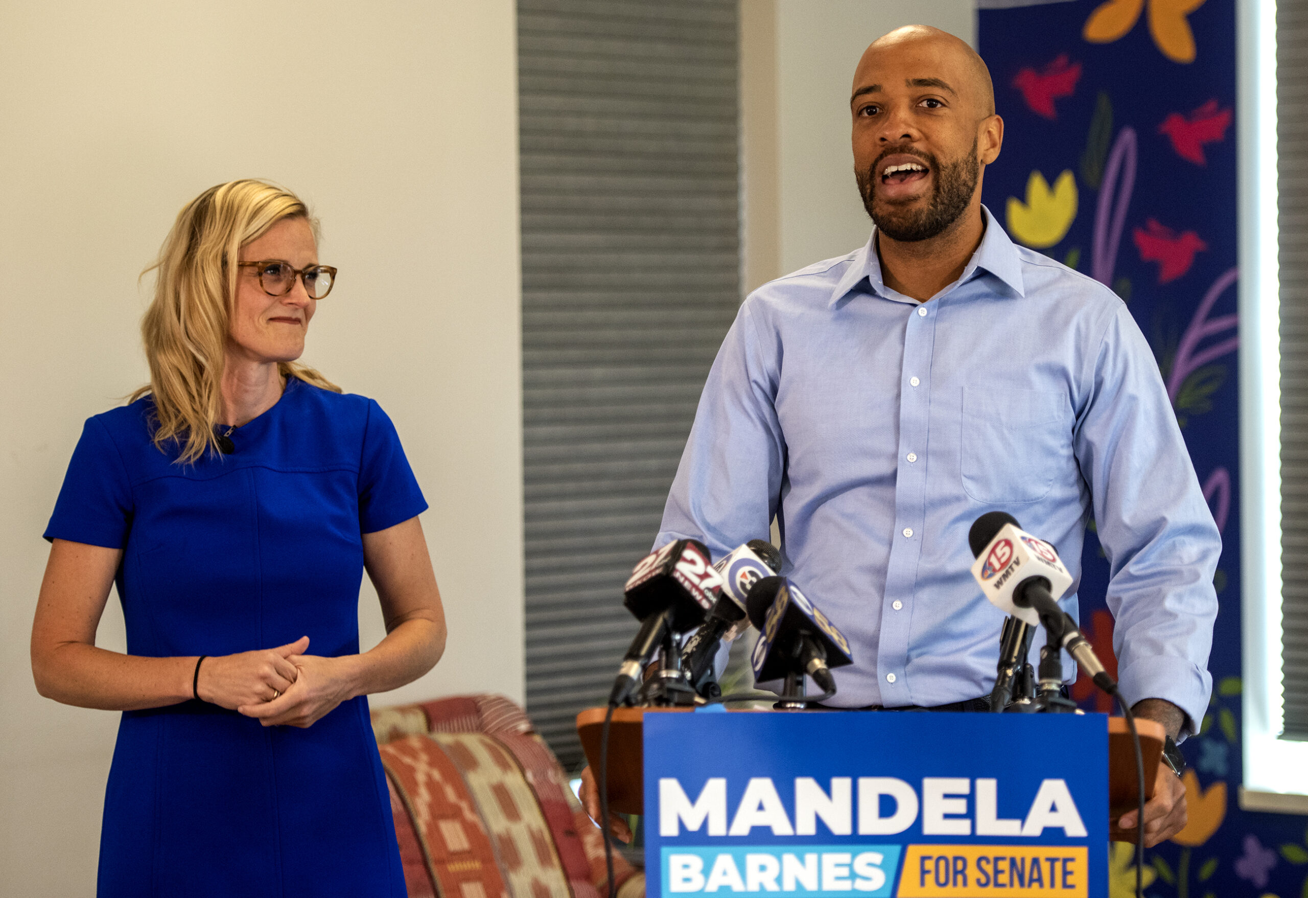 Sarah Godlewski looks over at Mandela Barnes as he speaks at a podium.