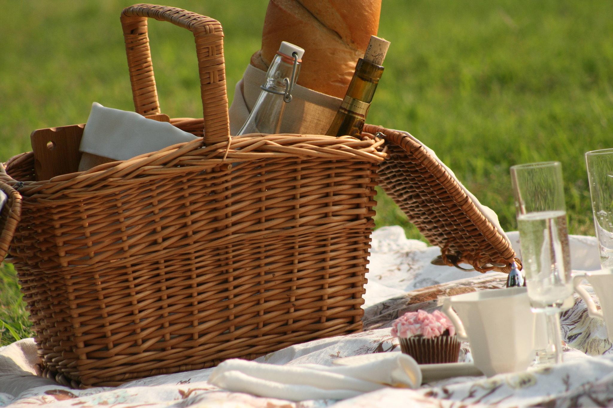 Picnic basket and champagne flutes on a blanket in grass