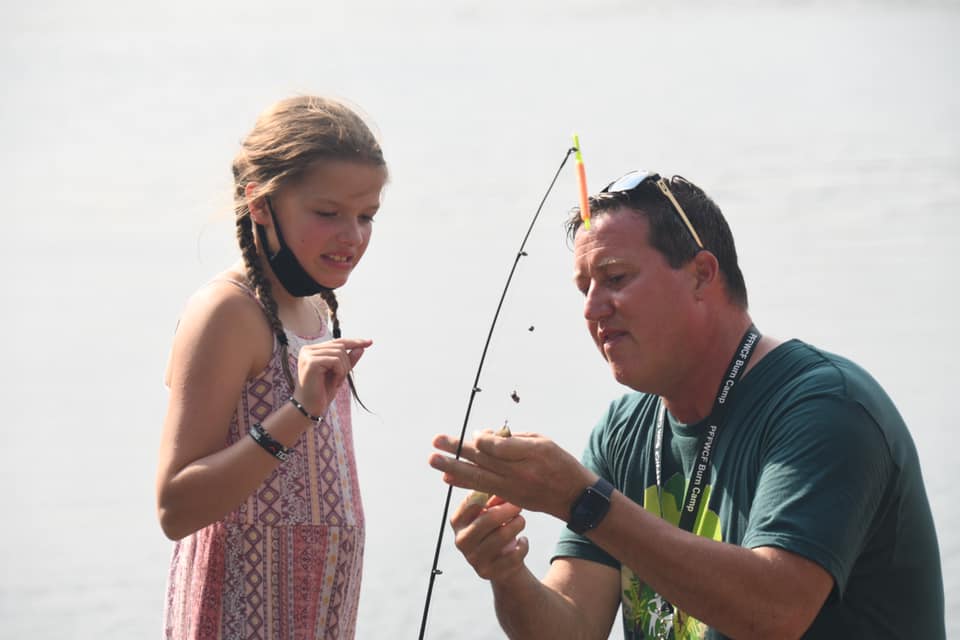 A camp volunteer helps a child with fishing