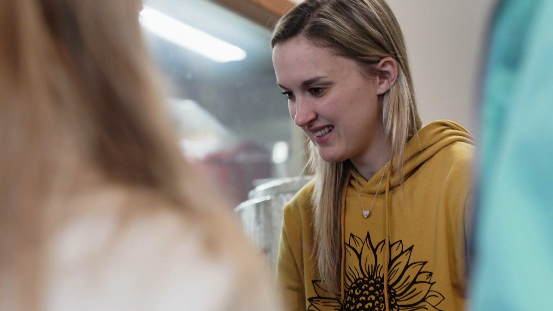 A woman wearing a yellow sweatshirt with a sunflower on it speaks with a customer